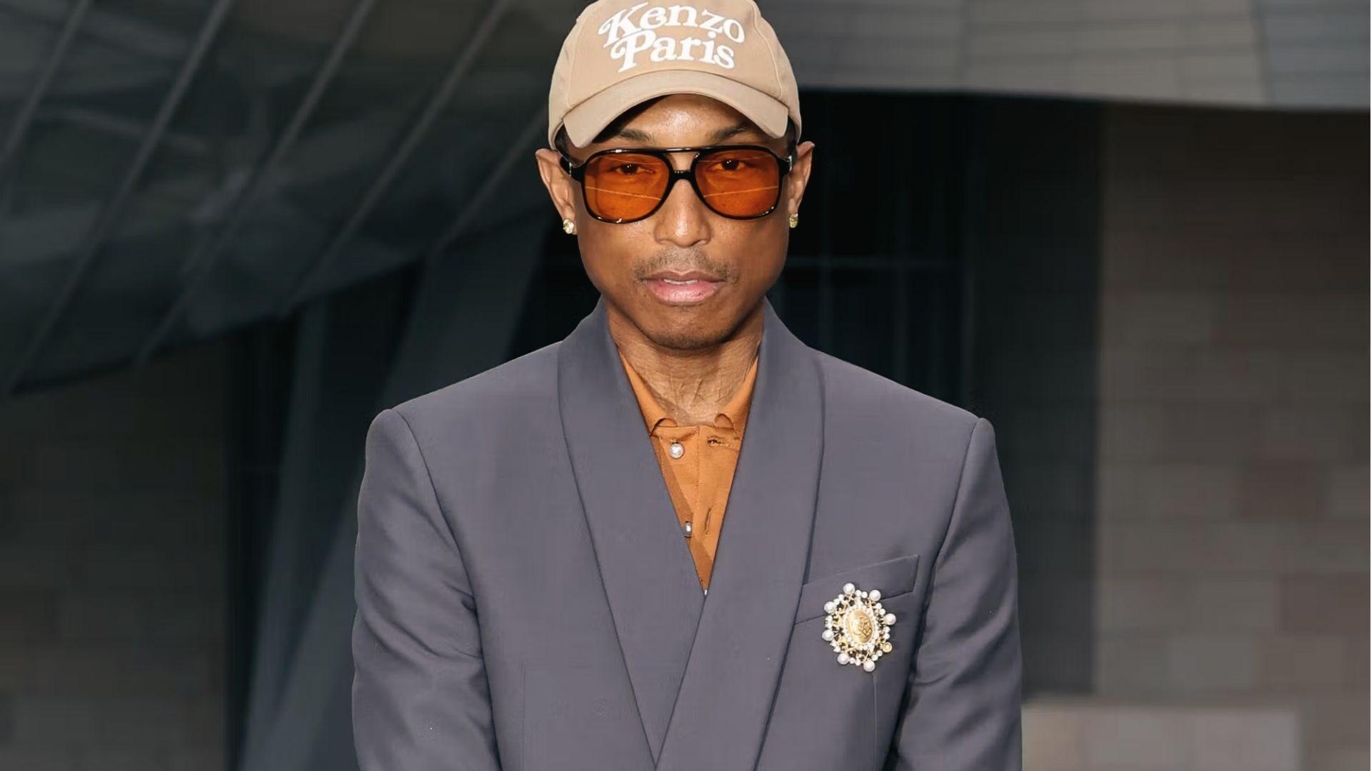 Pharrell Williams in gray suit, Kenzo Paris cap, orange shirt, pearl brooch, amber sunglasses