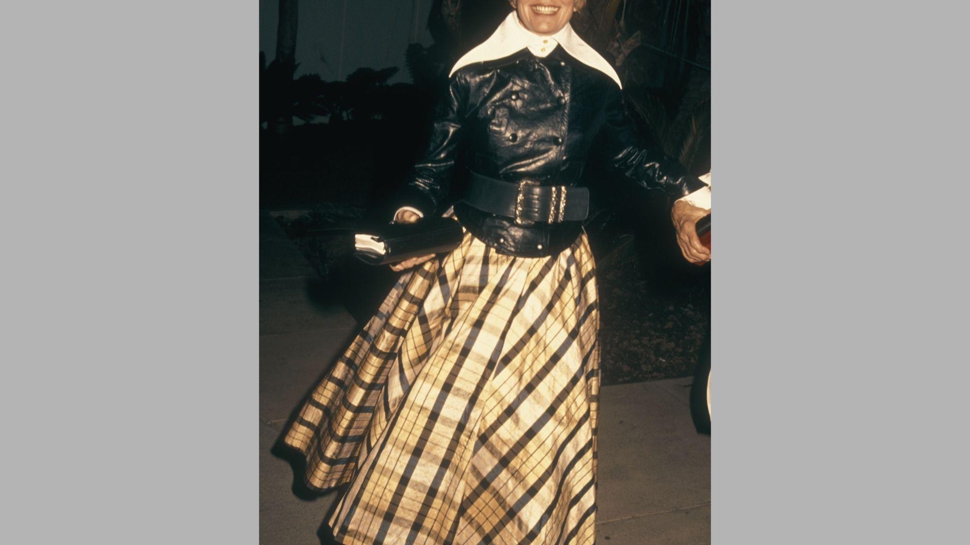 Vintage photo of smiling woman in leather jacket and plaid skirt holding books outdoors