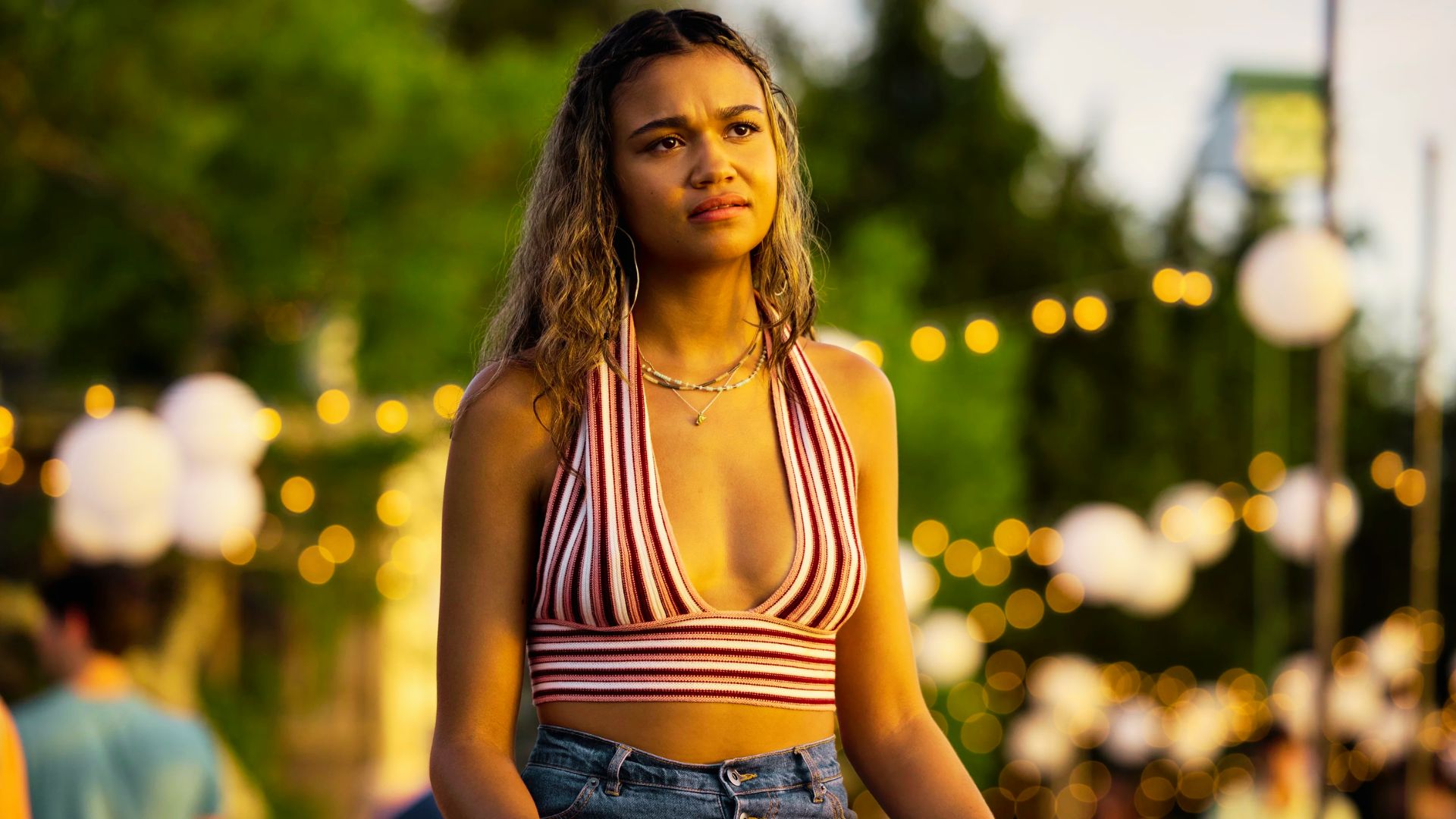 Kiara stands outdoors at golden hour in a red and white striped halter crop top and high-waisted jeans.
