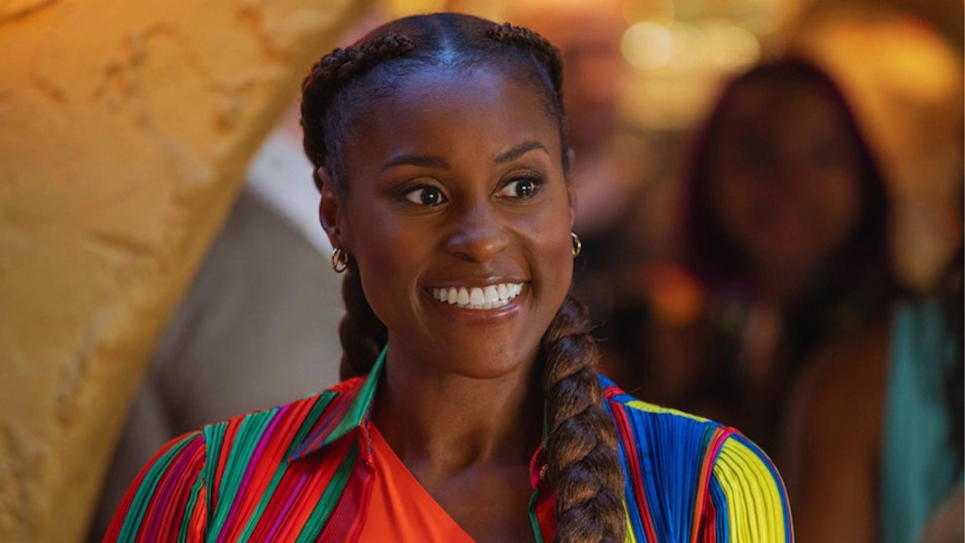 Issa Rae smiles with a thick side braid and twisted crown, wearing a colorful striped top.