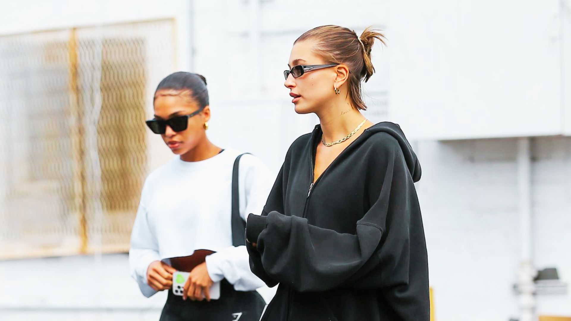 Hailey Bieber walks with a friend in a casual black oversized zip-up hoodie and matching pants.