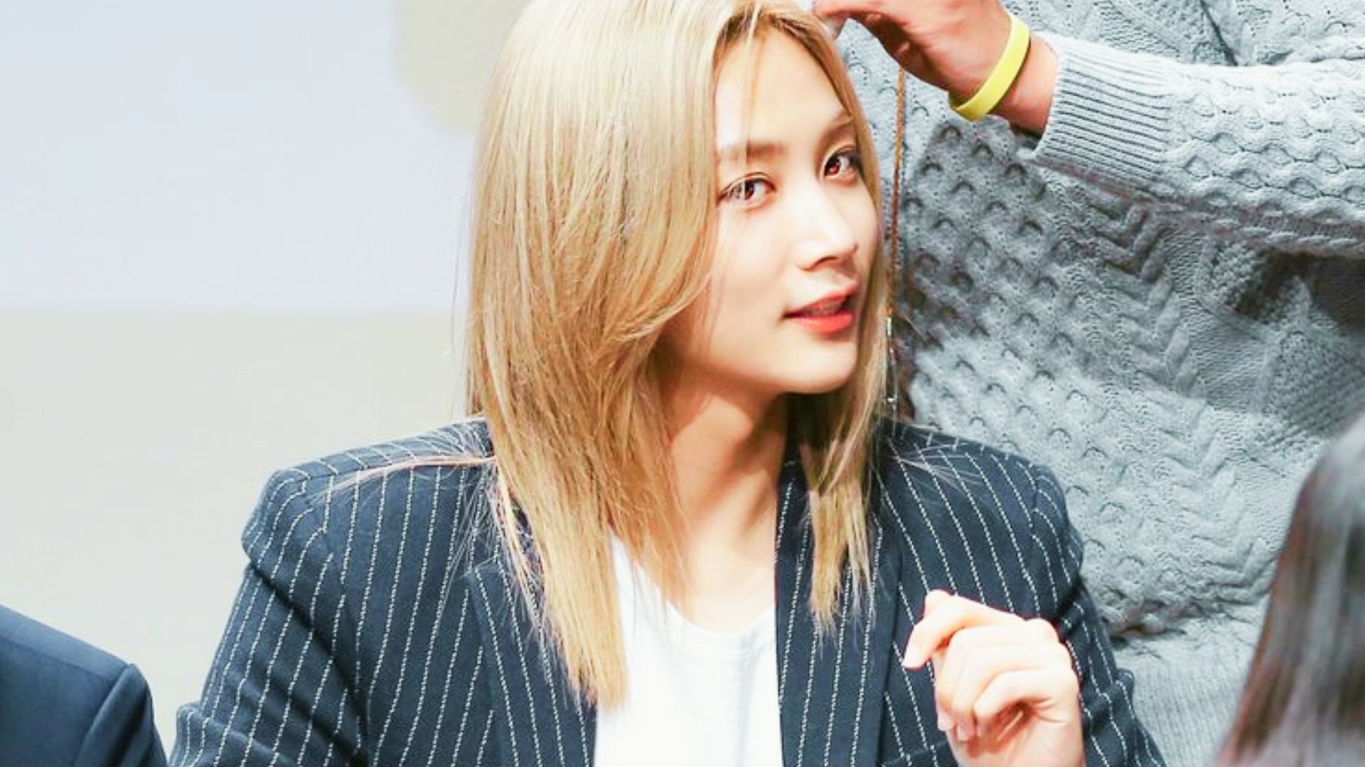 Jeonghan in a pinstripe blazer at a fansign, long blonde hair parted to the side.
