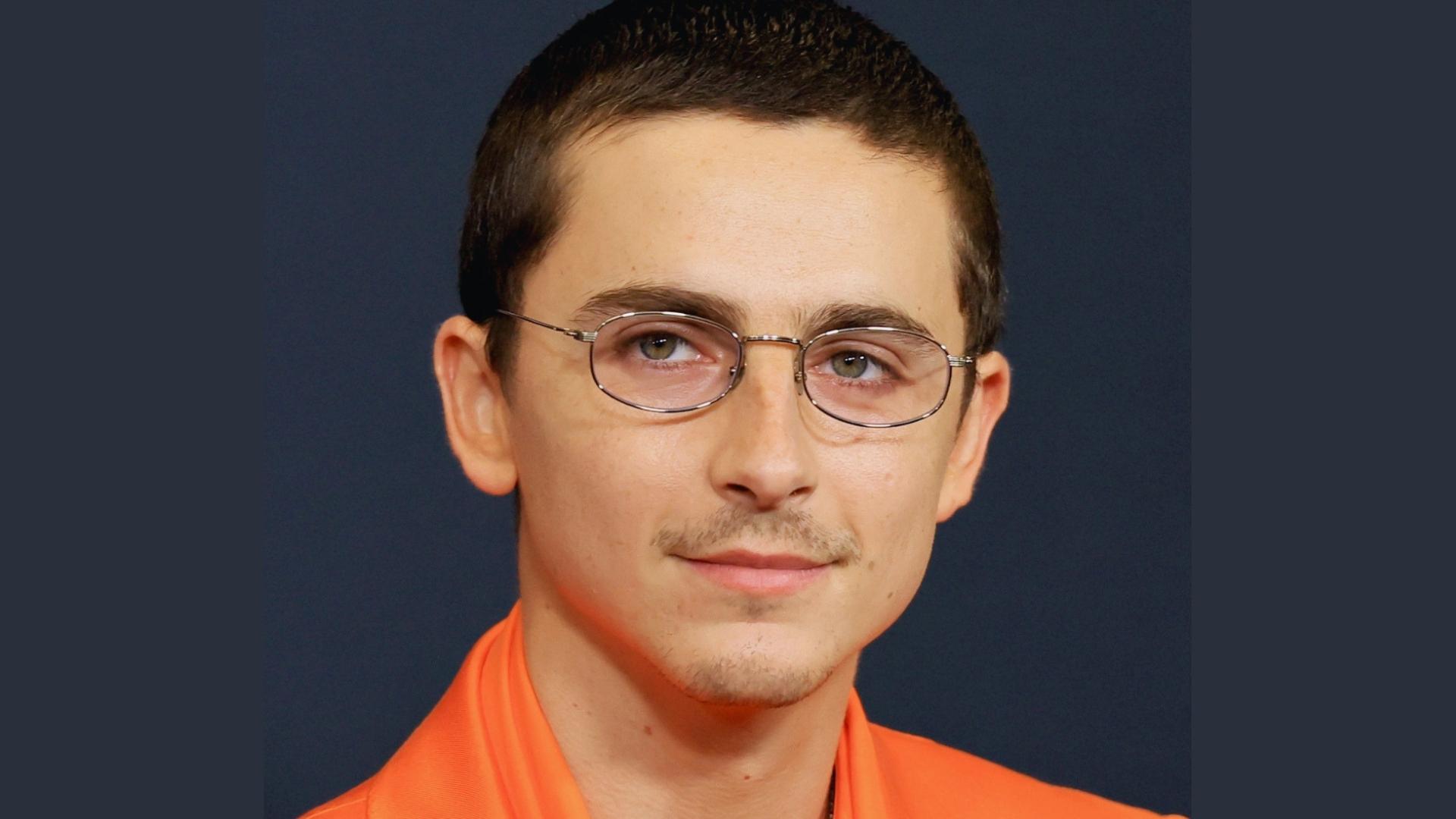 Timothée Chalamet shows off his neat buzz cut and glasses on the red carpet, styled with a subtle mustache.