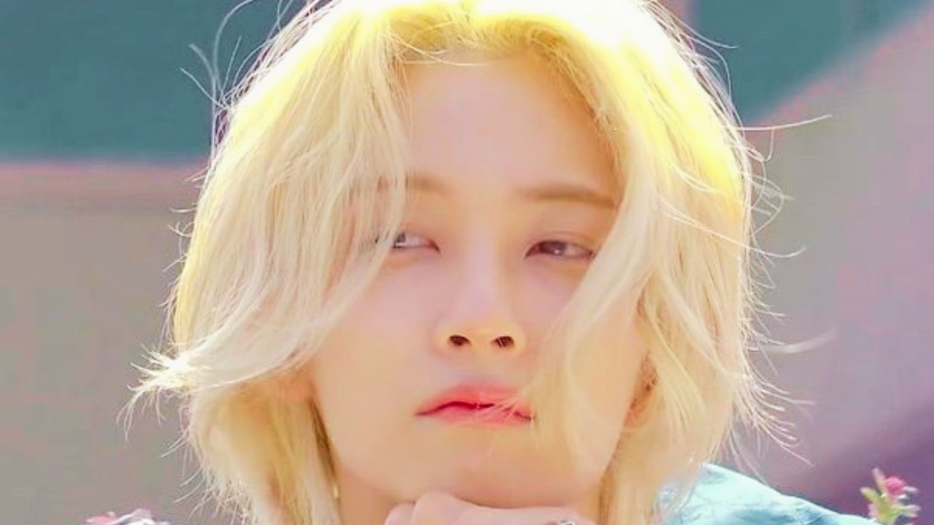 Stage shot of Jeonghan smiling with slicked-back platinum blonde hair and in-ear monitors.