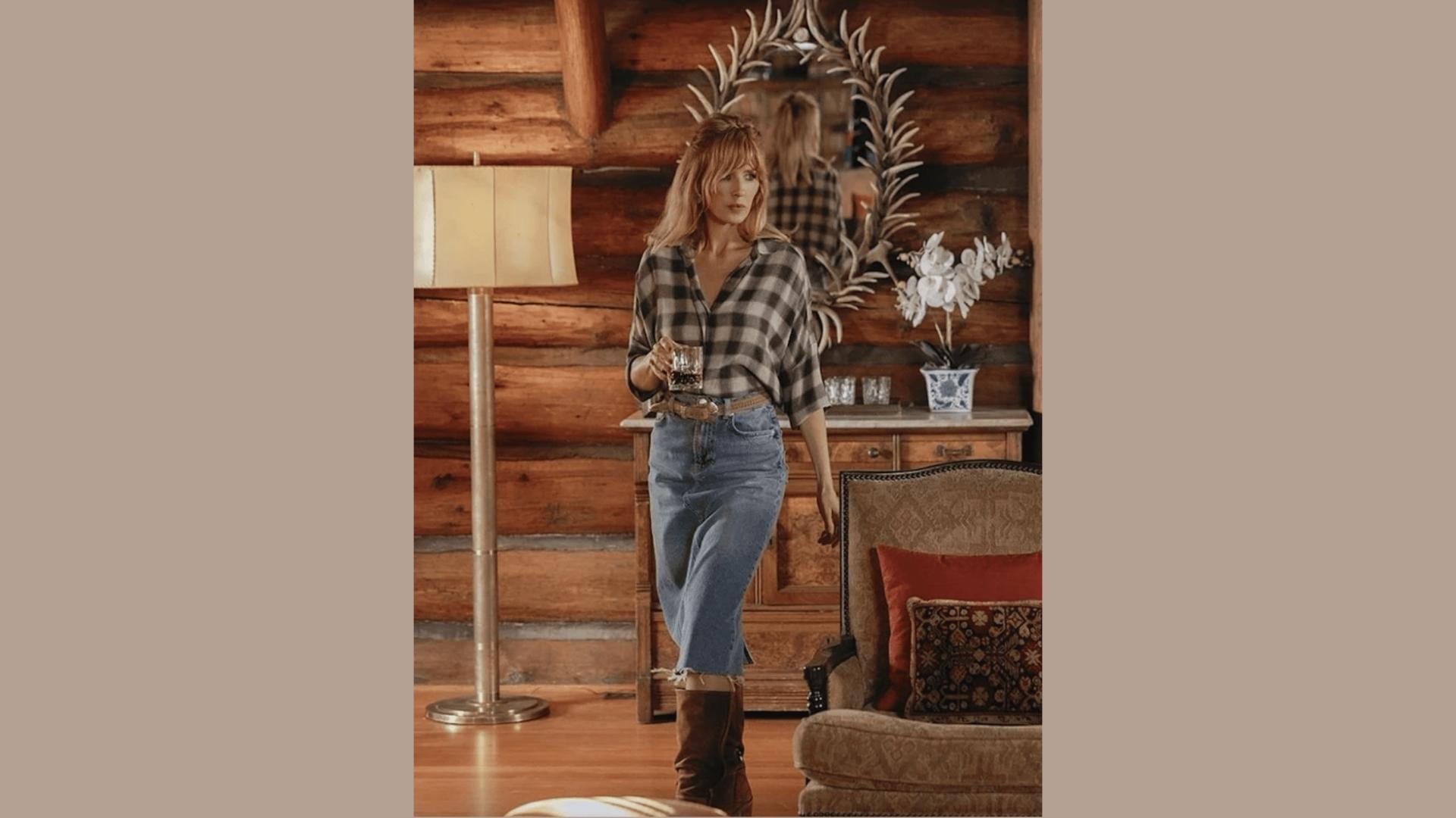 Beth Dutton stands in a log cabin wearing oversized black plaid shirt, denim midi skirt, and brown cowboy boots..
