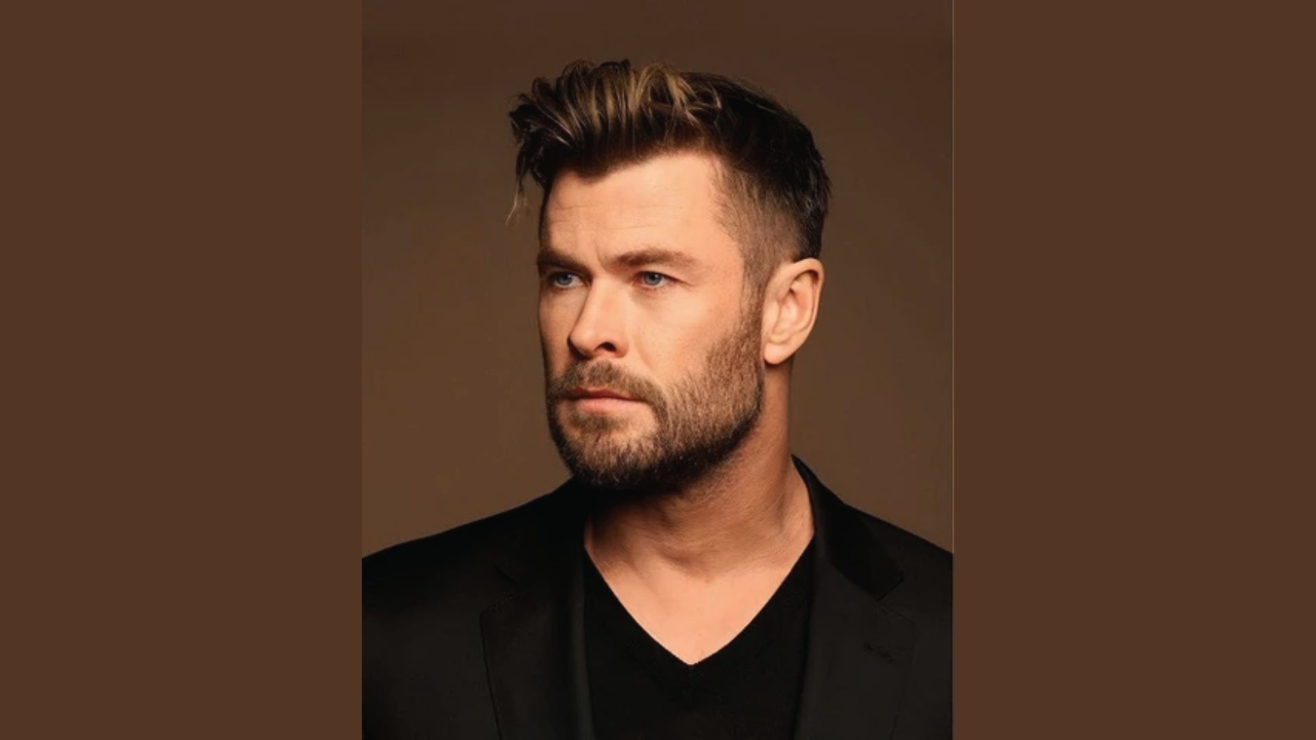Chris Hemsworth with a beard wearing a black shirt, showcasing a classic side part hairstyle for inspiration.