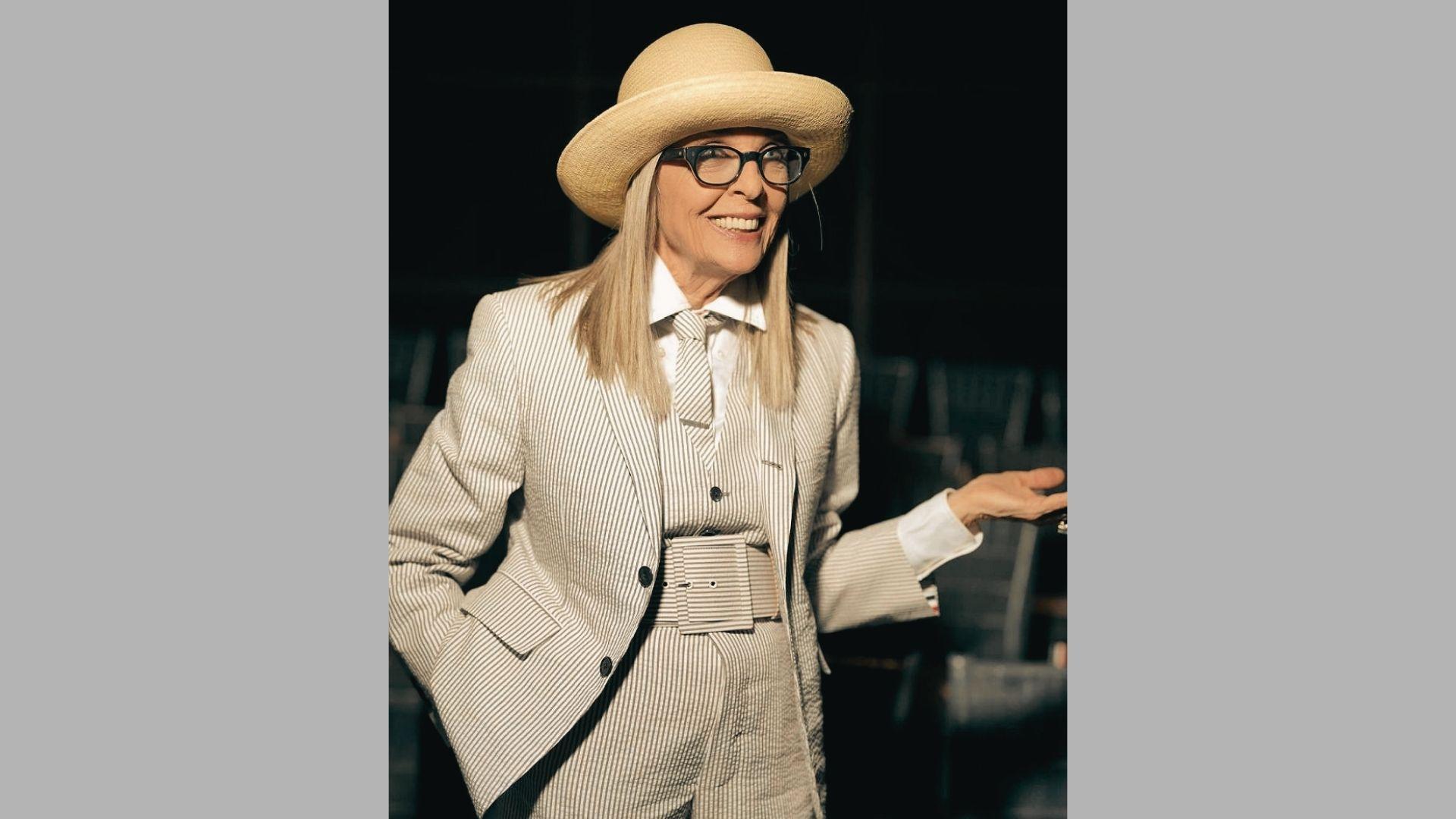 Smiling woman in striped suit, straw hat, and tie gestures while speaking at event