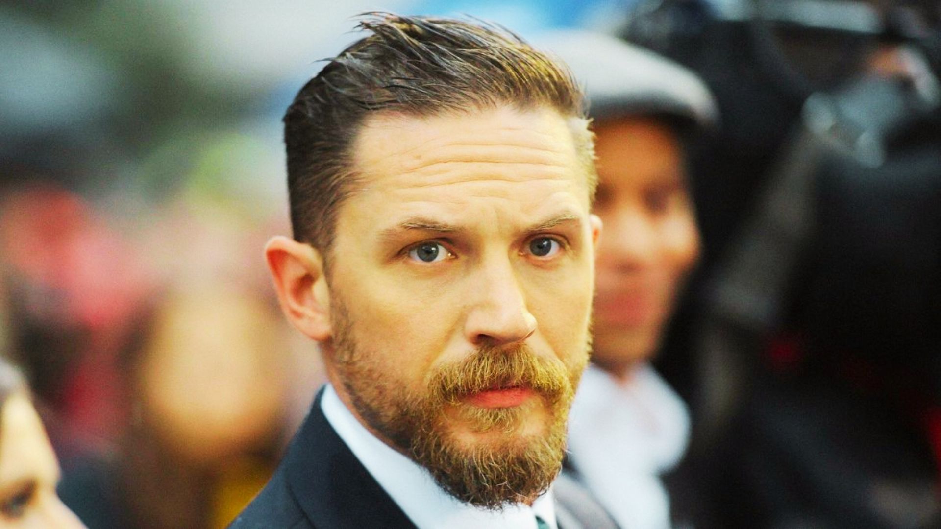 Tom Hardy at a red carpet event with a high-shine slicked back undercut and full beard.