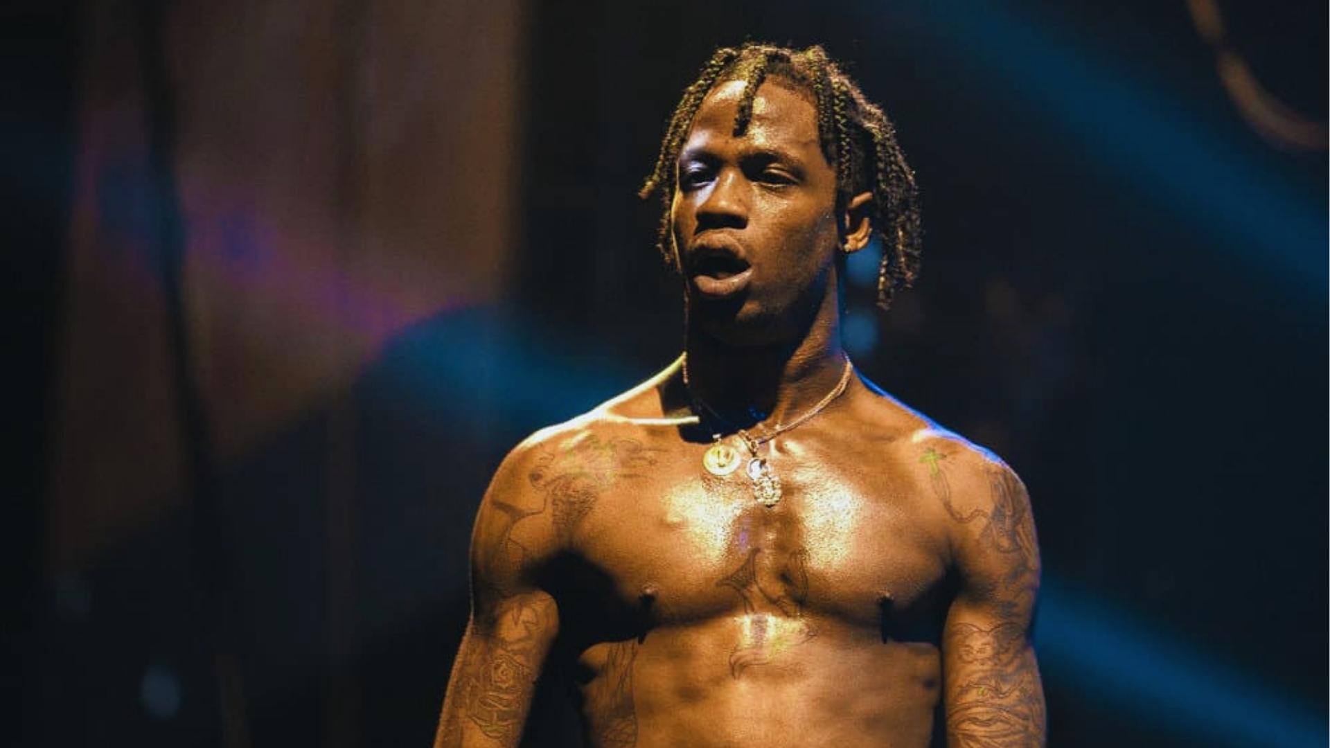Travis Scott performs shirtless on stage with short twisted locs, showcasing his signature freeform braided look.