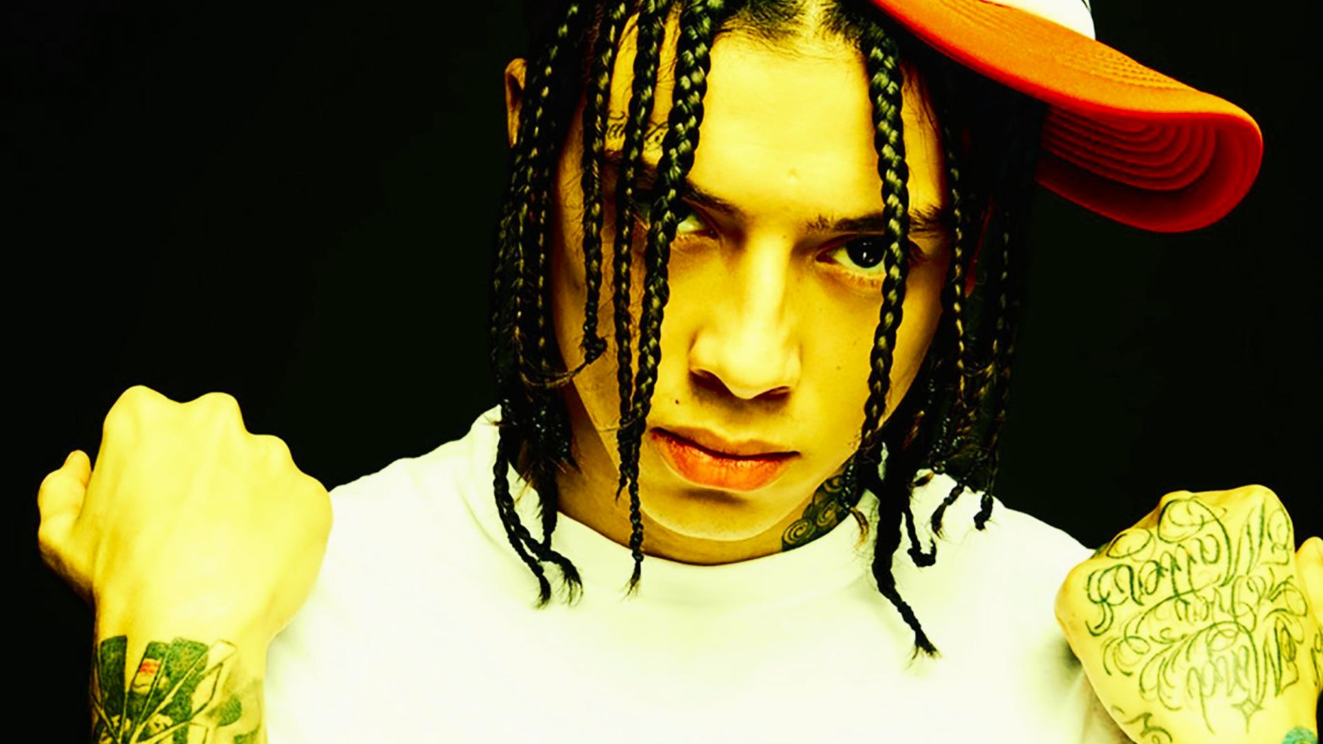 Central Cee wears a red and white cap, rocking long thin box braids that fall over his face.
