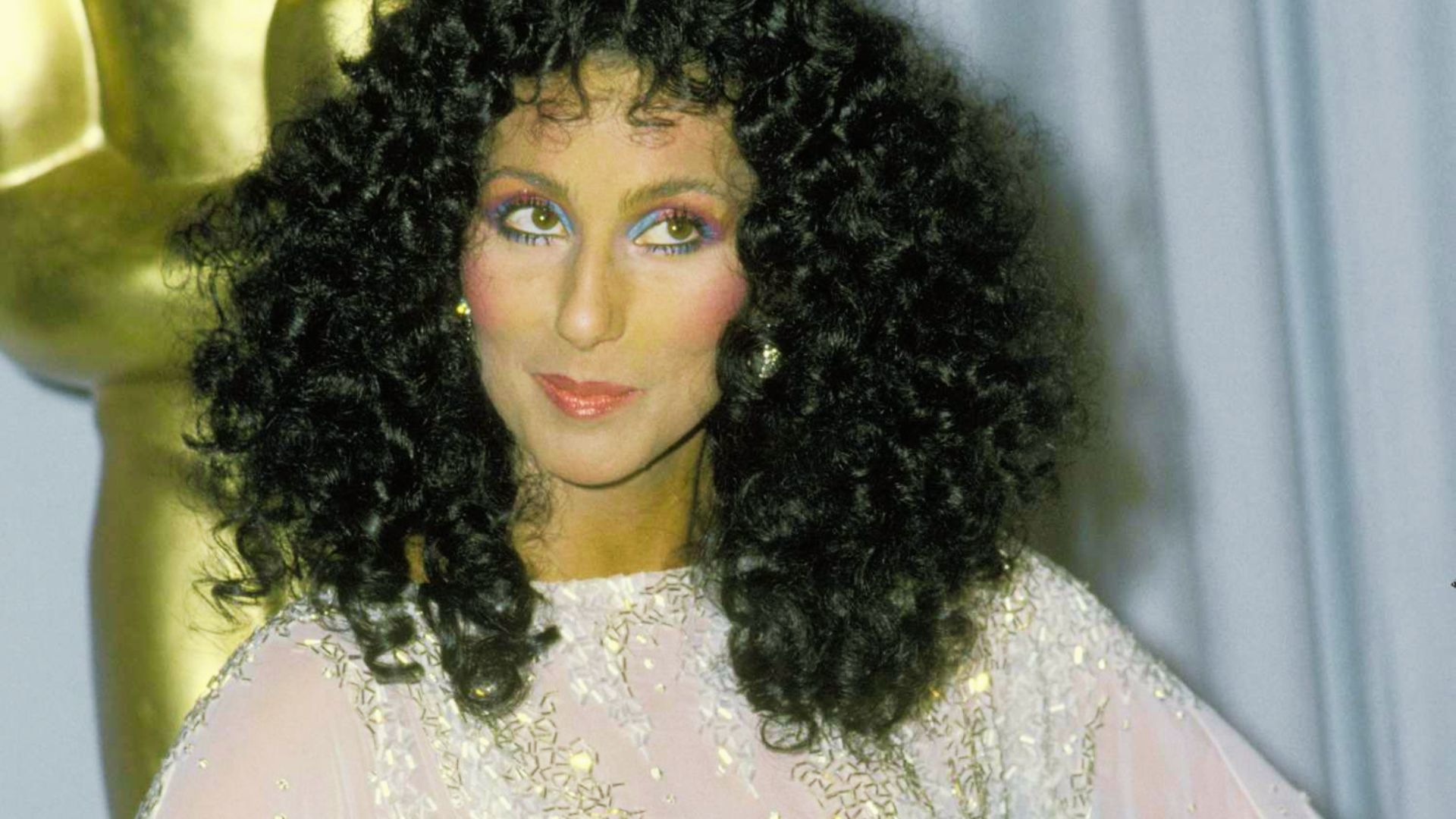 Cher at the 1974 Oscars in a pale pink Bob Mackie gown with gold sequin detailing.