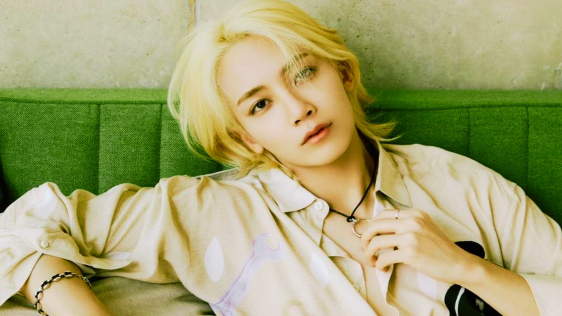 Jeonghan reclining on a green couch, tousled blonde hair spread around his face.