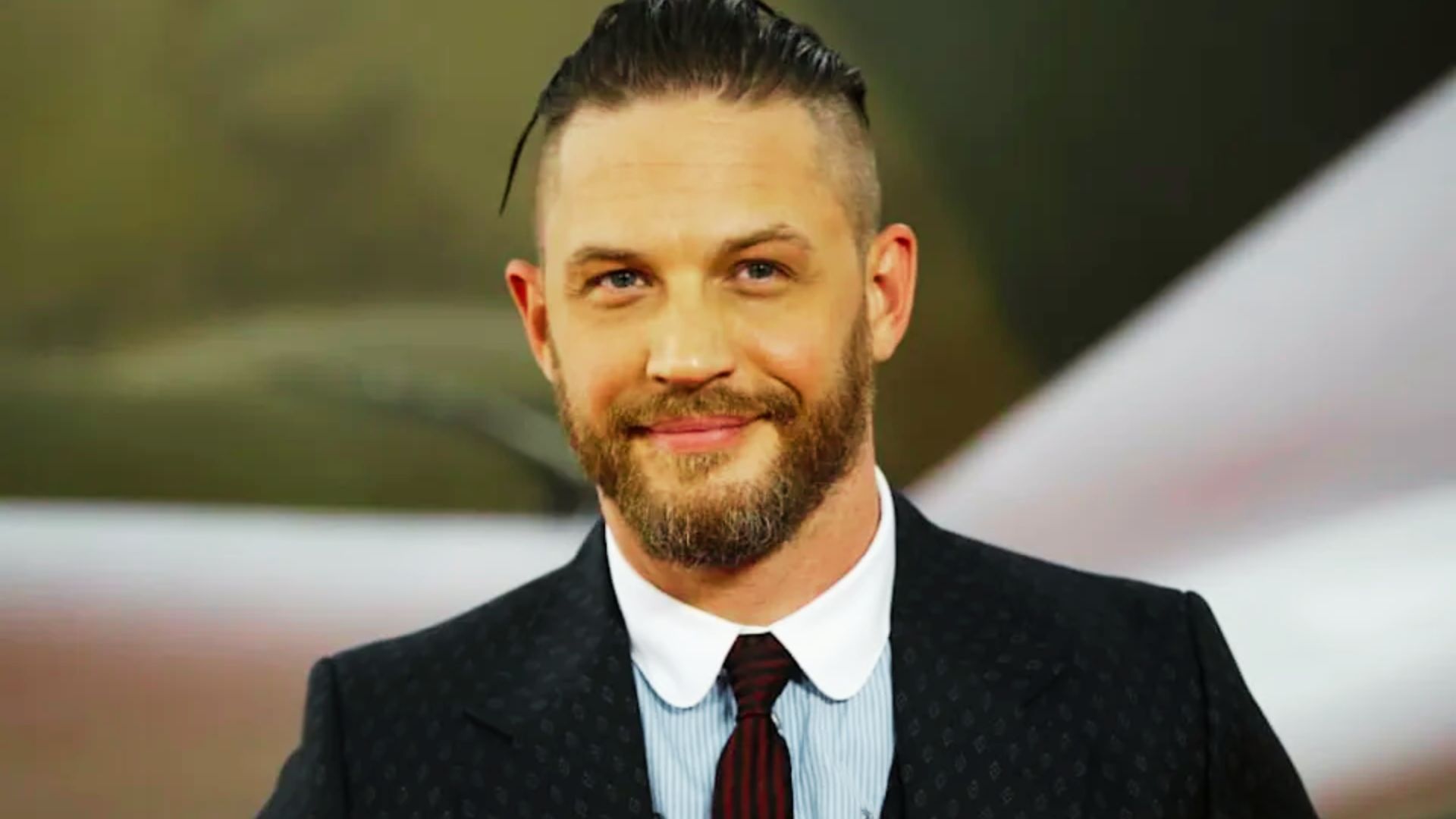 Tom Hardy in a tight crew cut with skin-faded sides and a full, groomed beard.