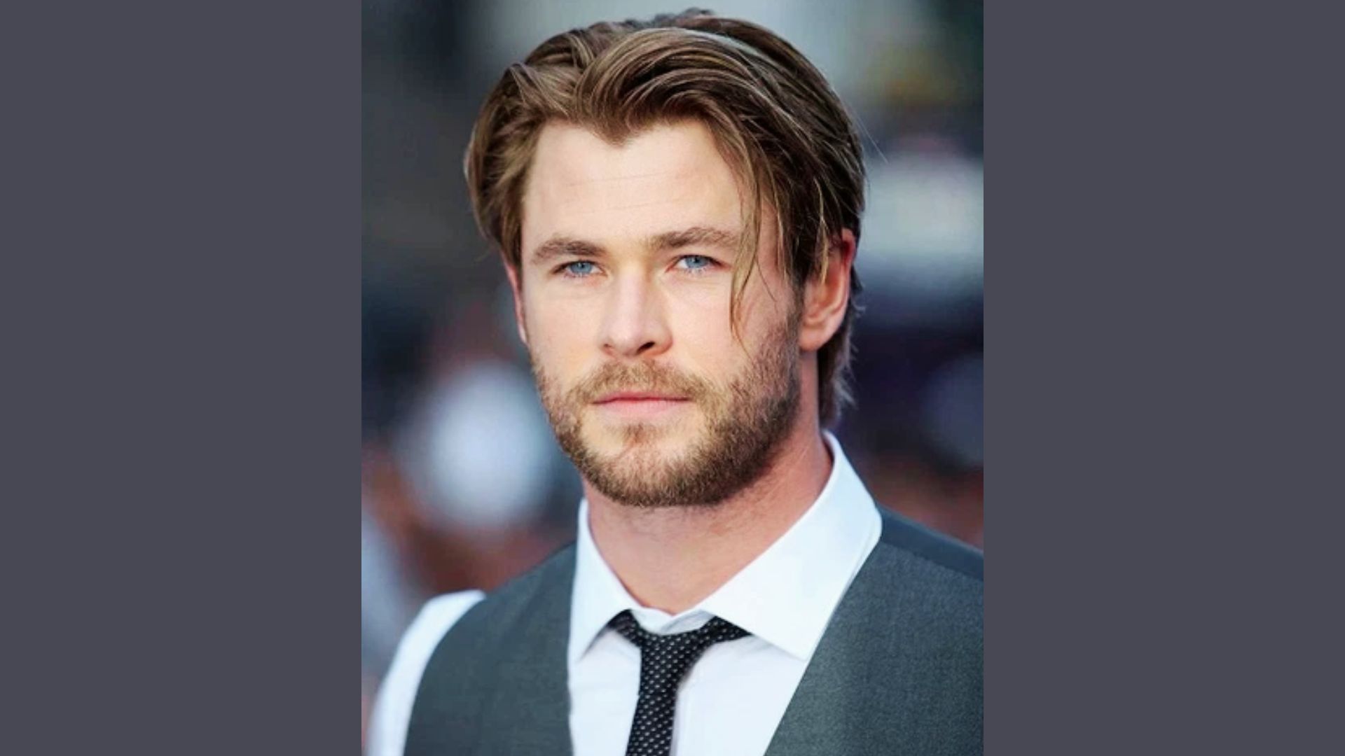 Chris Hemsworth in a tie gazes at the camera, showcasing a layered medium-length hairstyle for inspiration.