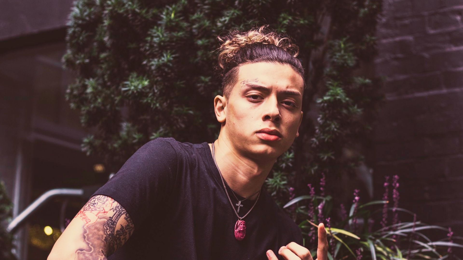 Central Cee outdoors in a black tee, with a man bun on top and faded sides, his curls tied up loosely.