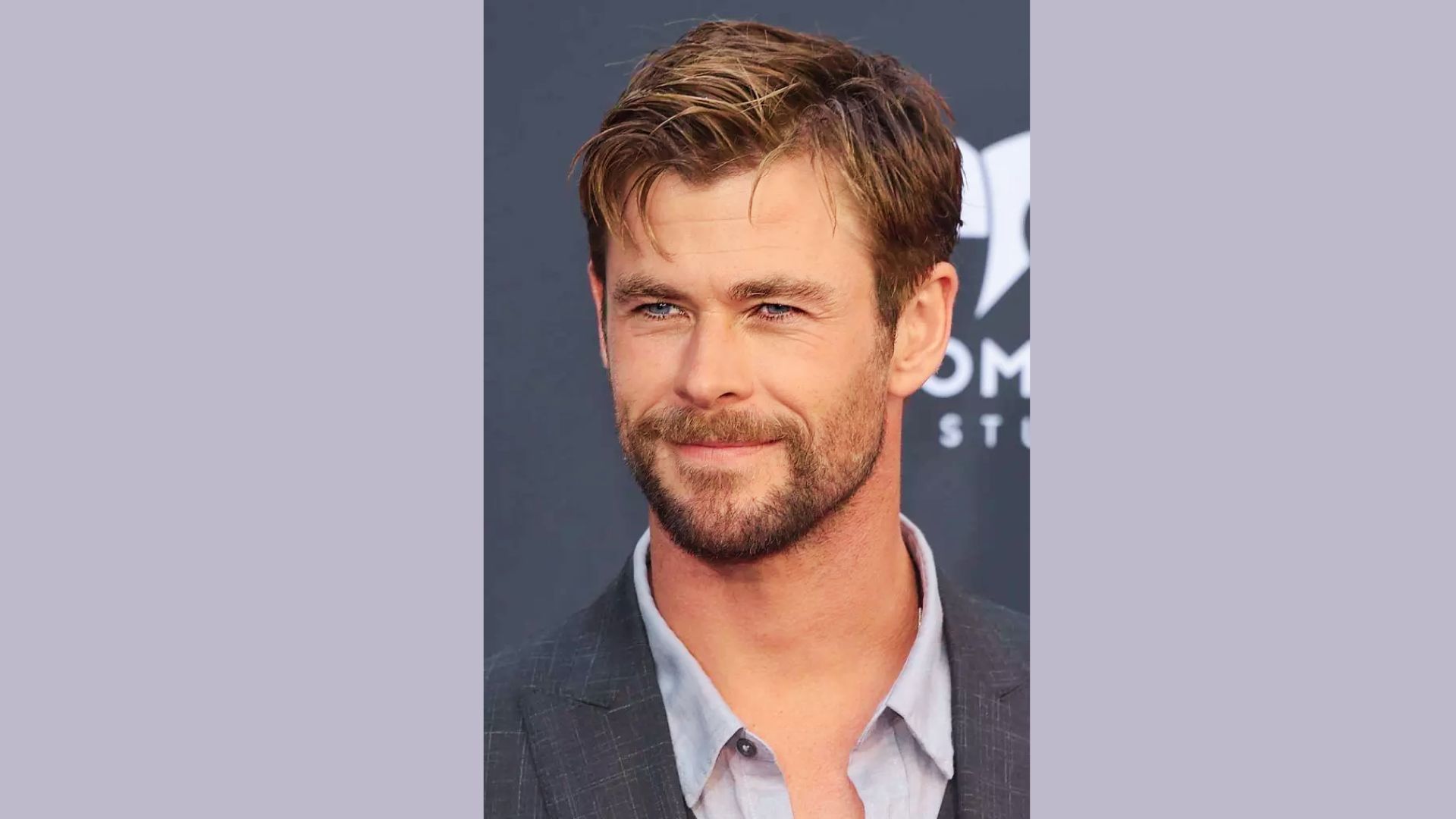 A man in a suit with a beard, displaying a Chris Hemsworth-style undercut with longer hair on top for hairstyle inspiration.
