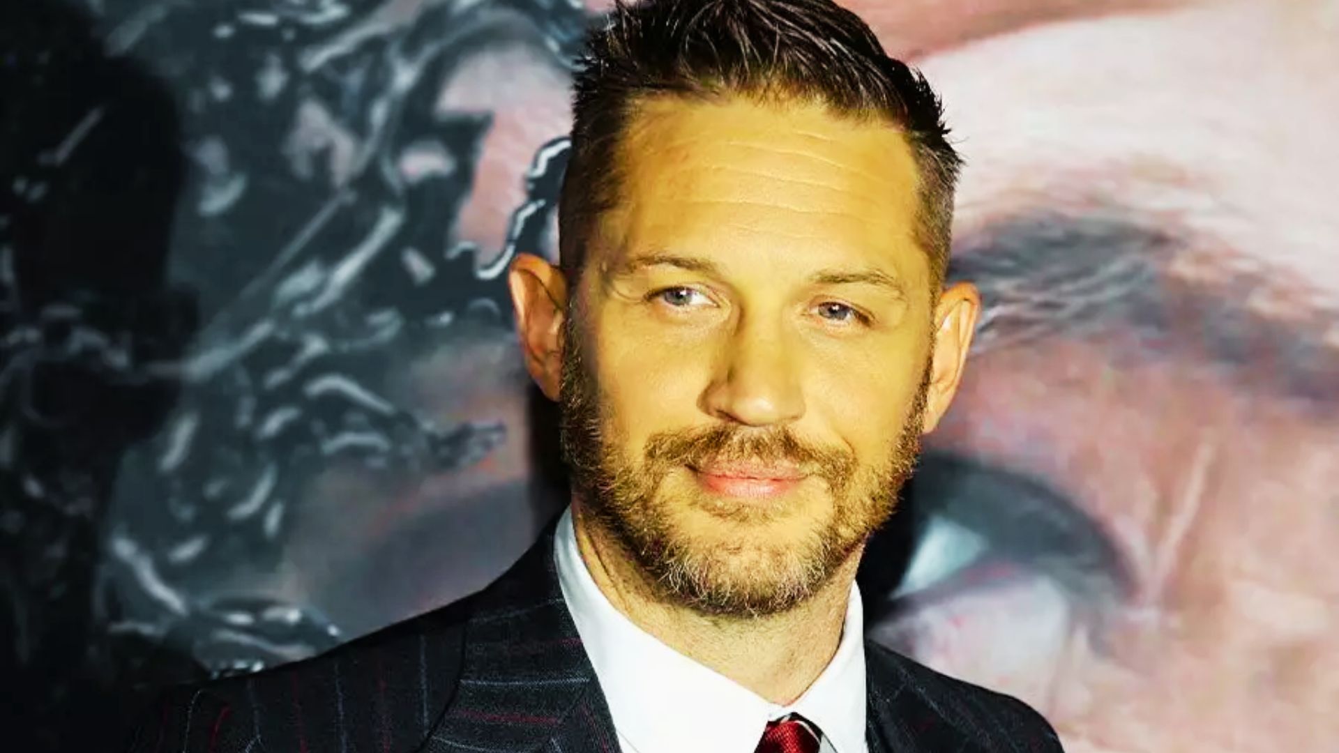 Tom Hardy at a red carpet event wearing a suit, with a slicked-back undercut and sharp side fade.