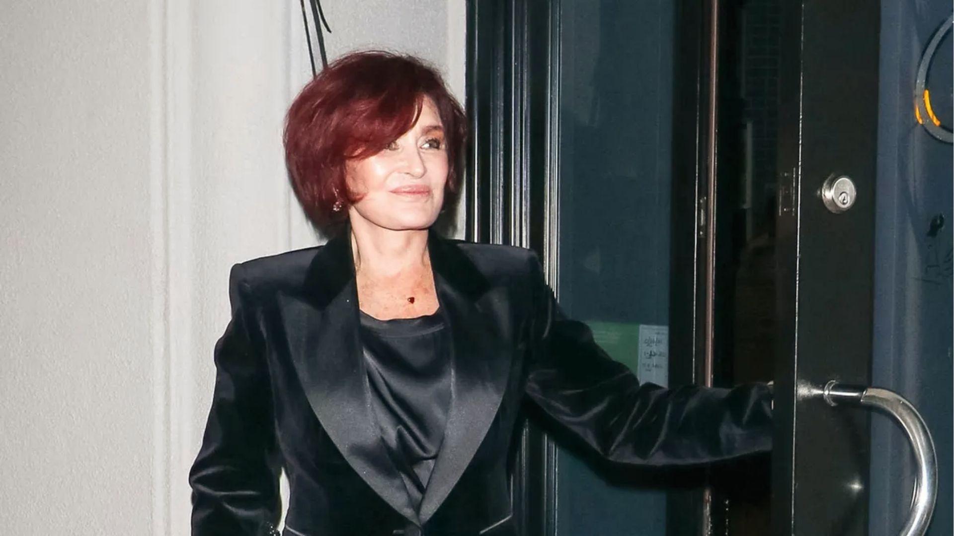 Sharon Osbourne exits in sleek black satin tuxedo blazer and heart necklace at night