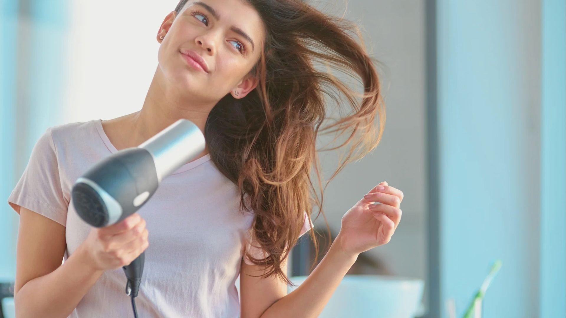 Woman blow-drying long brunette hair with a flip, creating movement and bounce.