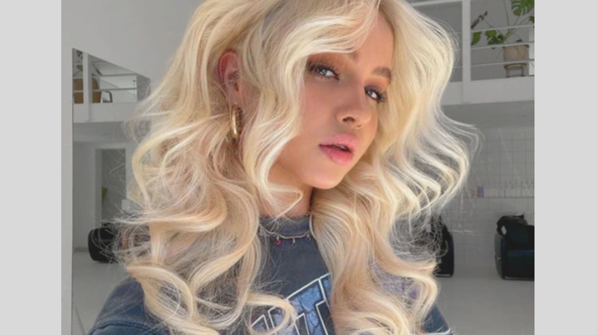 Close-up of ultra-voluminous platinum blonde curls with a deep side part and gold hoops.