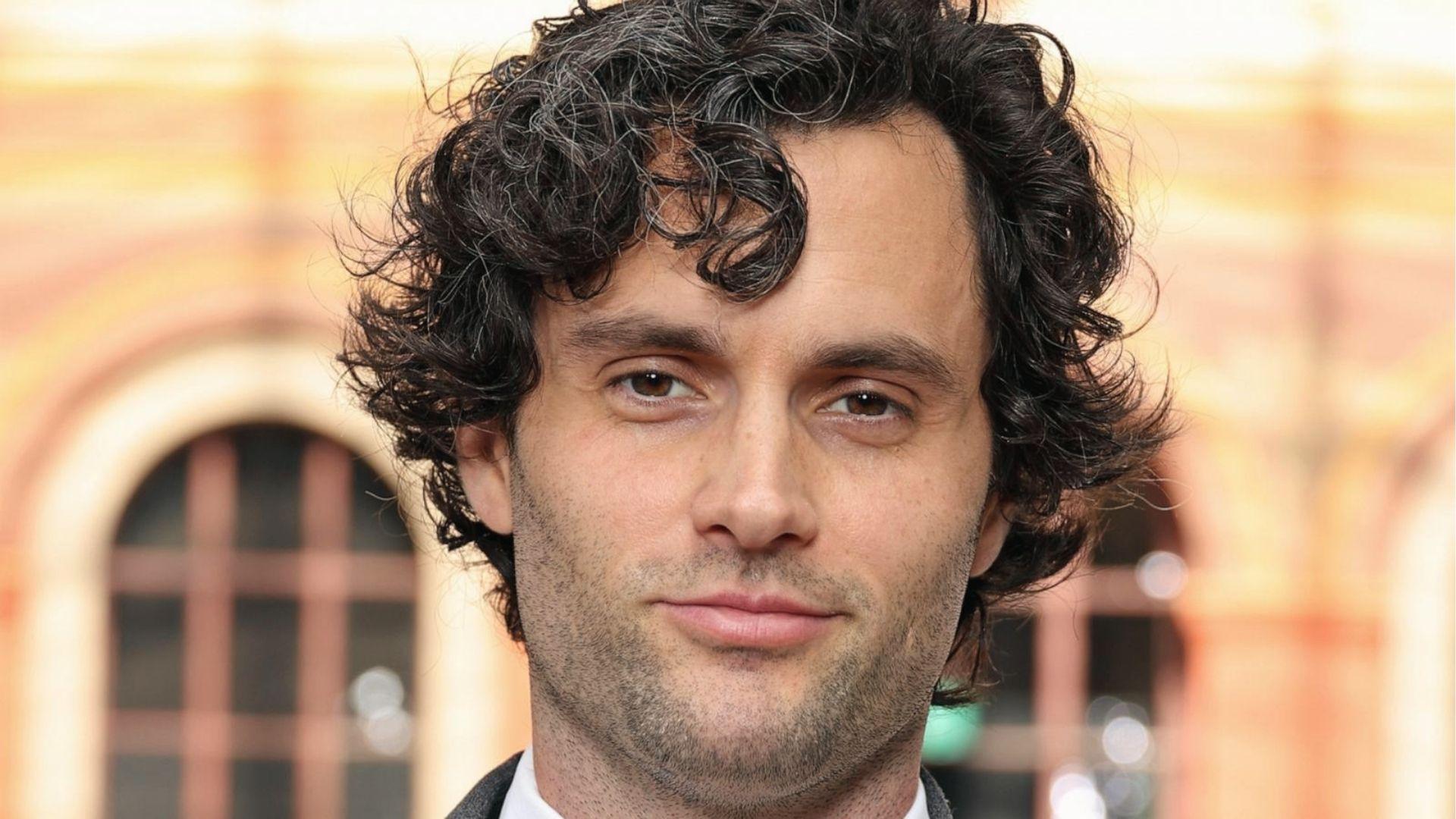 Penn Badgley shows tousled salt-and-pepper curls falling over forehead in a close-up shot.
