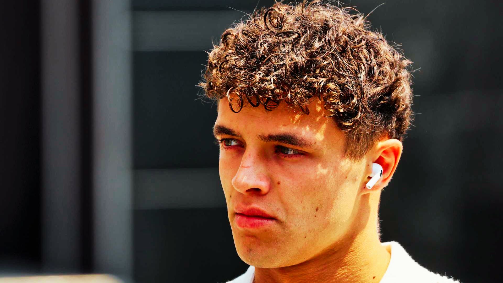 Close-up of Lando Norris wearing AirPods, with tight, defined curls.
