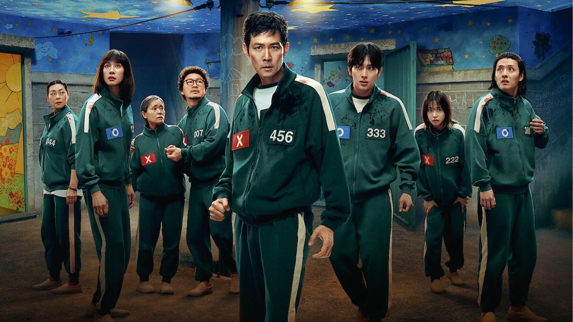 Cast of Squid Game in green tracksuits with number patches standing in a colorful game room.