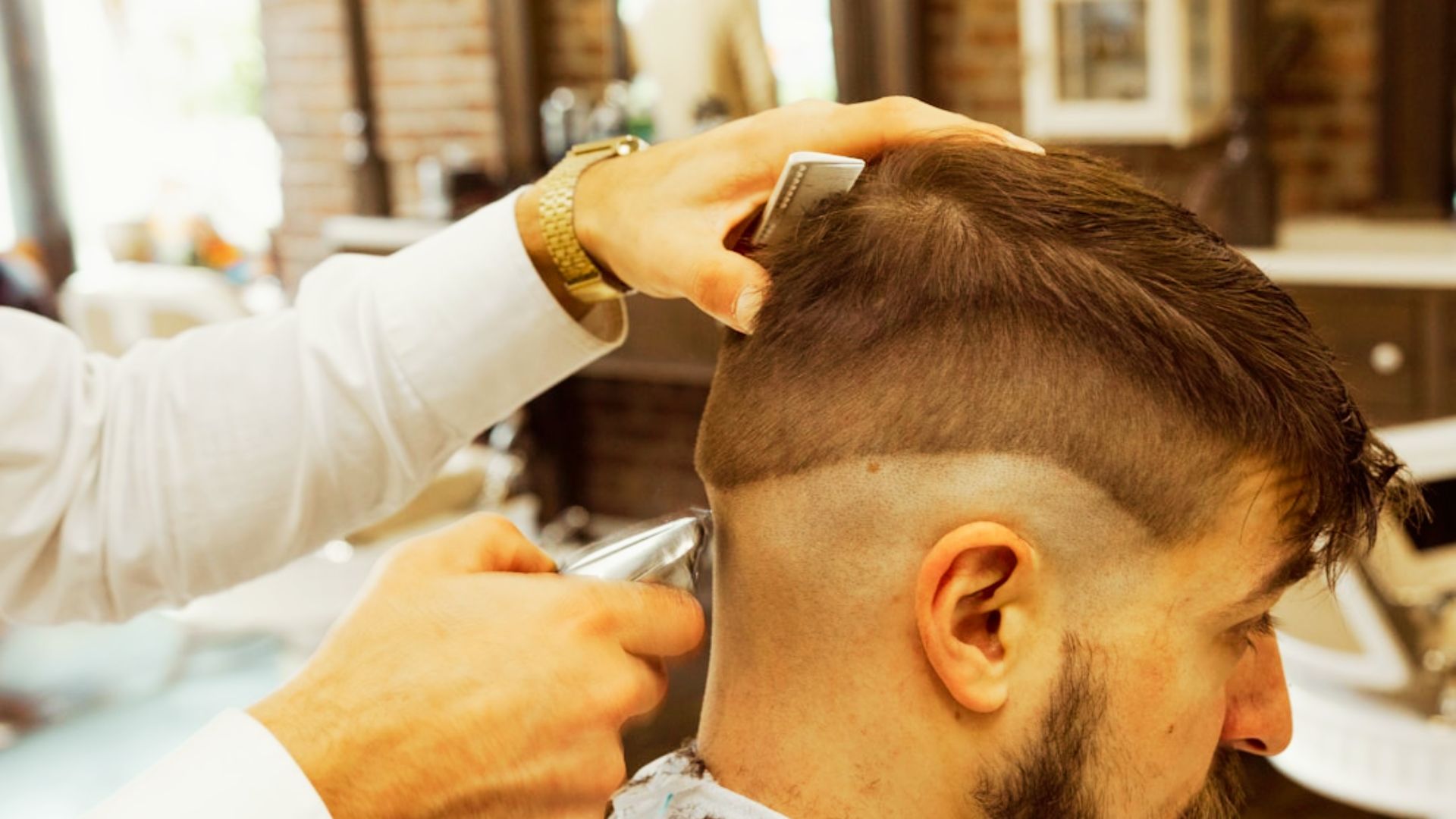 Barber using clippers to create a high skin fade on a client, with longer textured hair left on top.