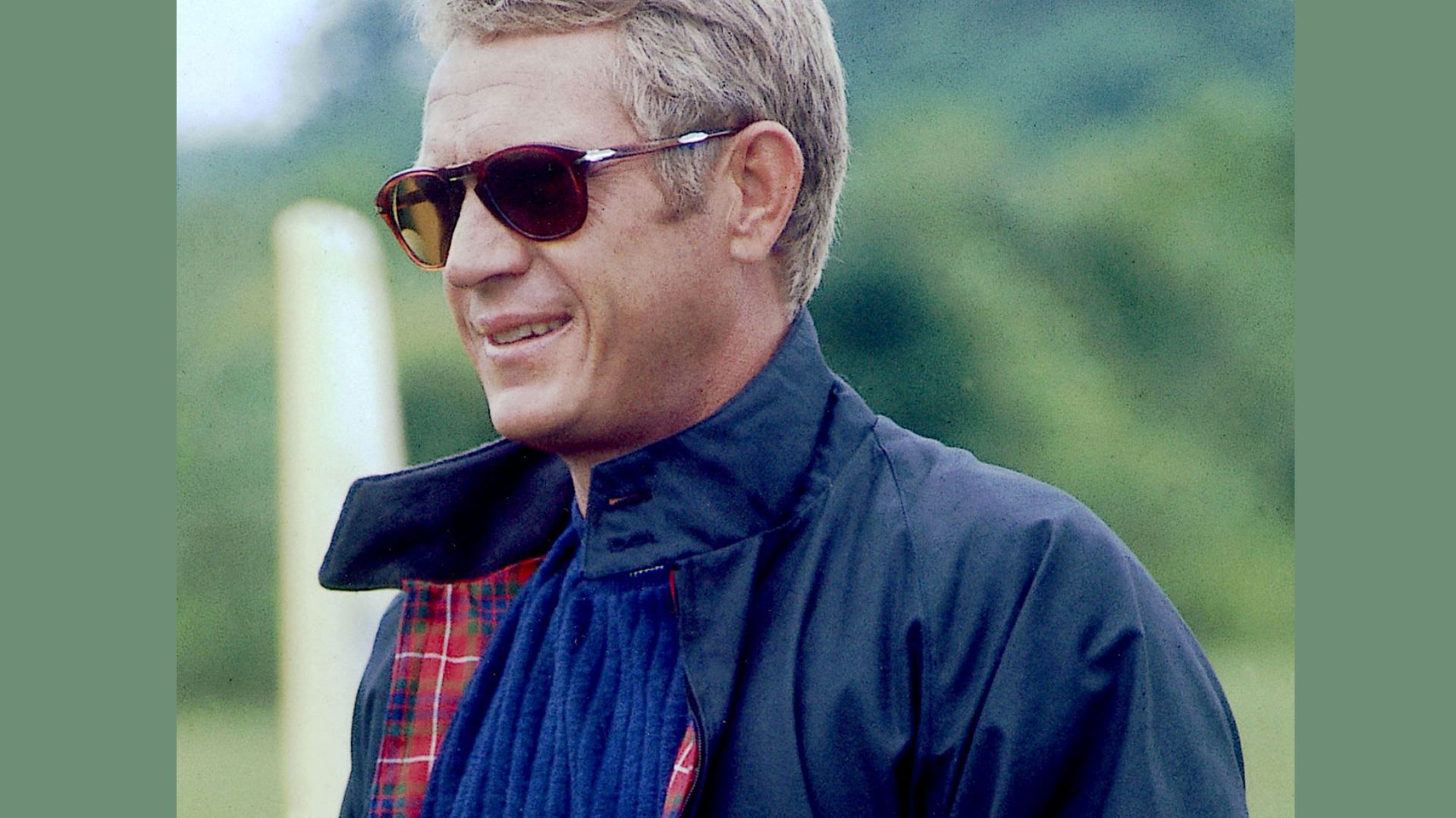 "A smiling man wearing sunglasses and a plaid shirt stands confidently, exuding a cheerful demeanor."