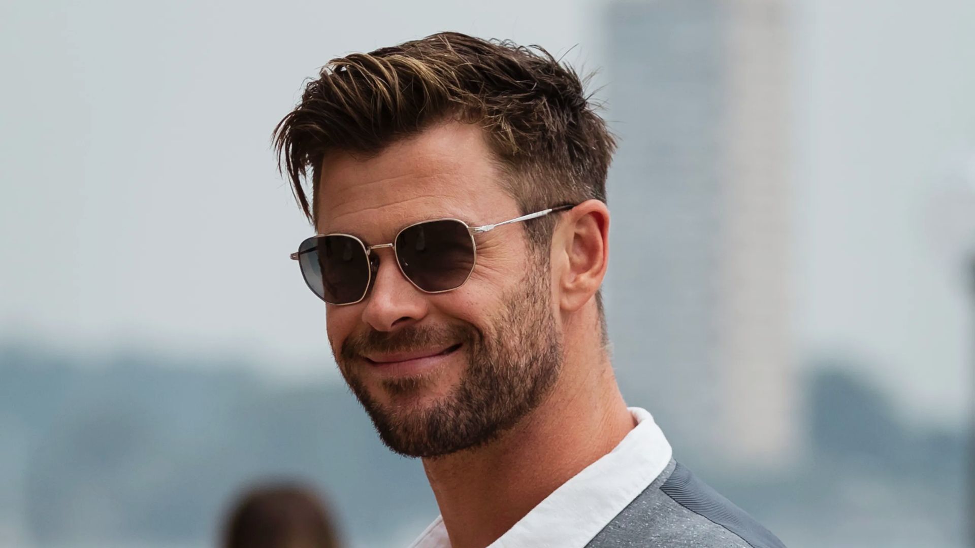 A man with sunglasses and a beard smiles, reminiscent of Chris Hemsworth, famous for his trendy haircuts.