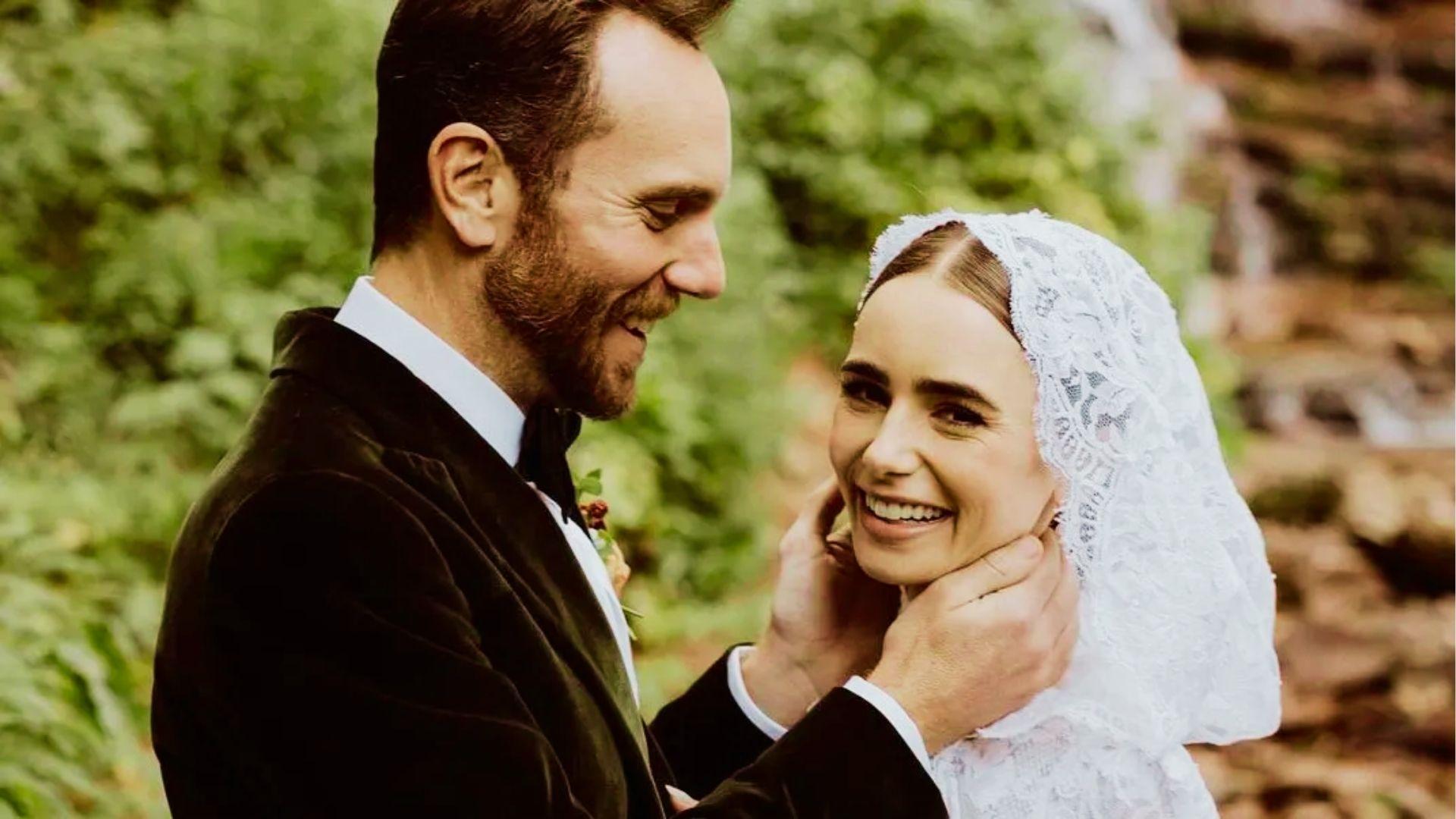 Smiling bride in lace hooded cape faces groom in velvet tuxedo outdoors by waterfall setting