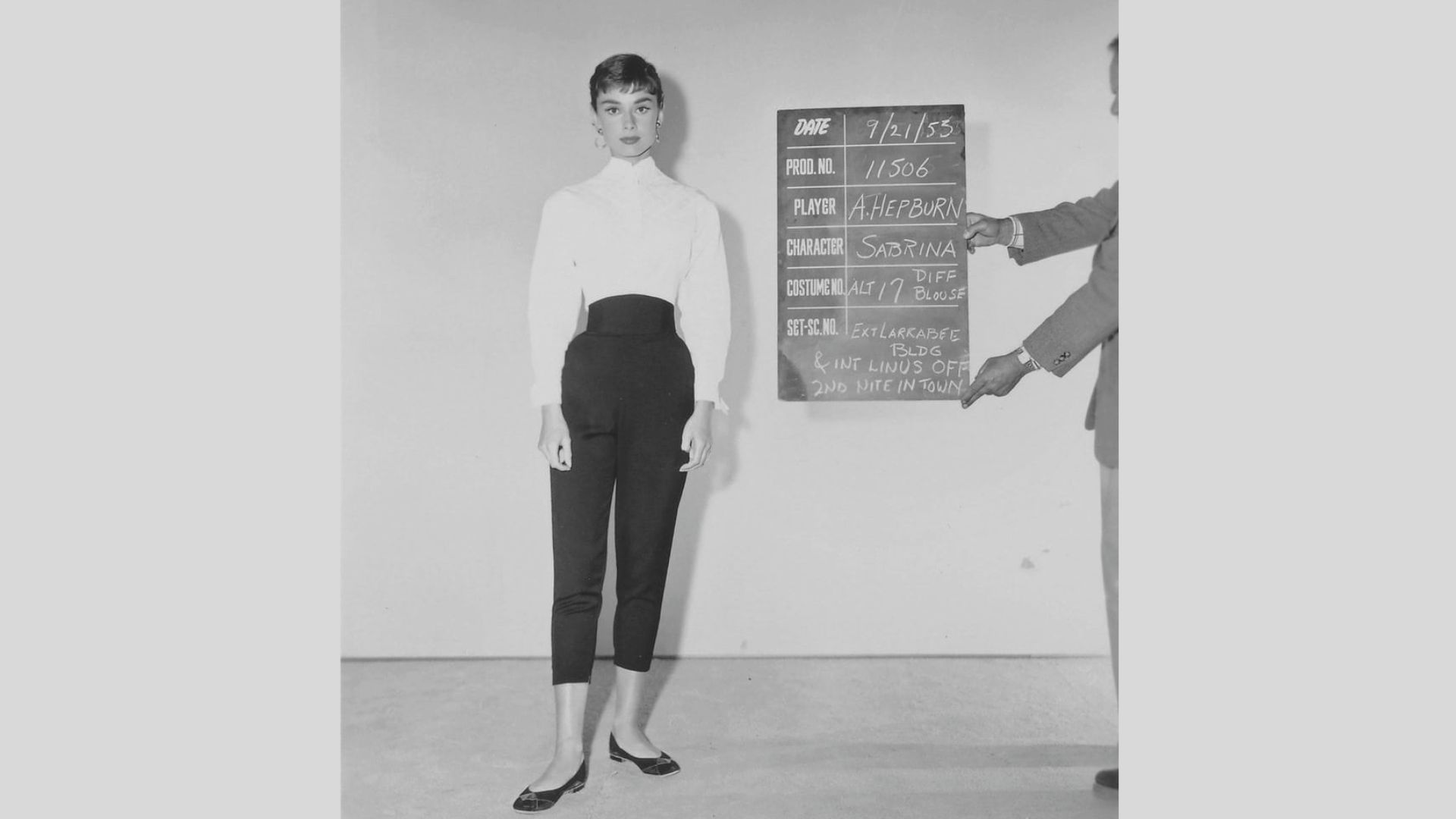 Wardrobe test photo for Sabrina shows Audrey Hepburn in a white high-neck blouse and slim black capri pants with ballet flats.