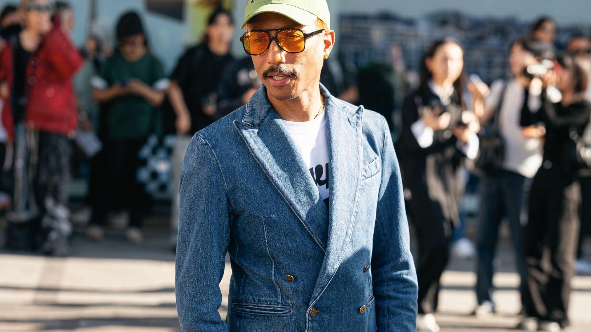 Pharrell Williams wears denim double-breasted blazer, white tee, green cap, amber sunglasses