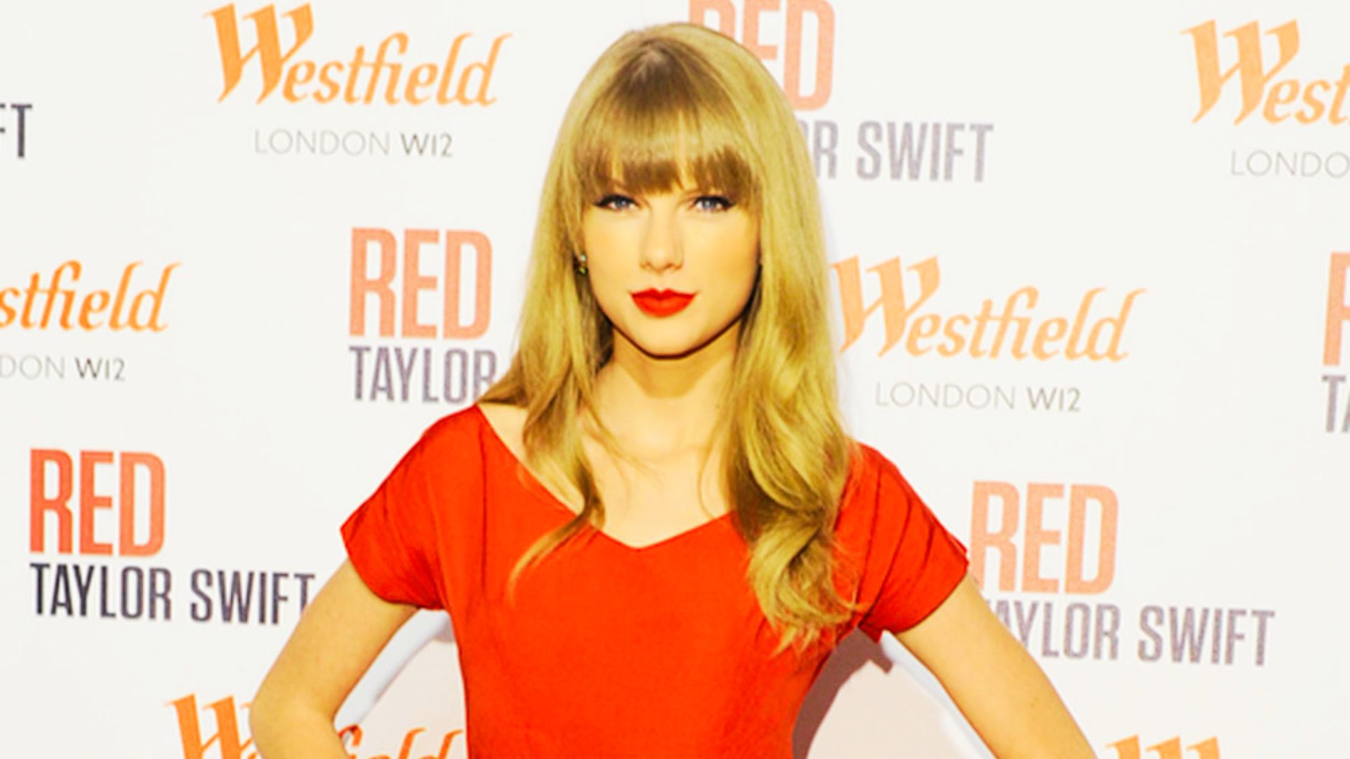 Taylor Swift poses at her Red album event with long, bright blonde hair styled in soft waves and blunt bangs.