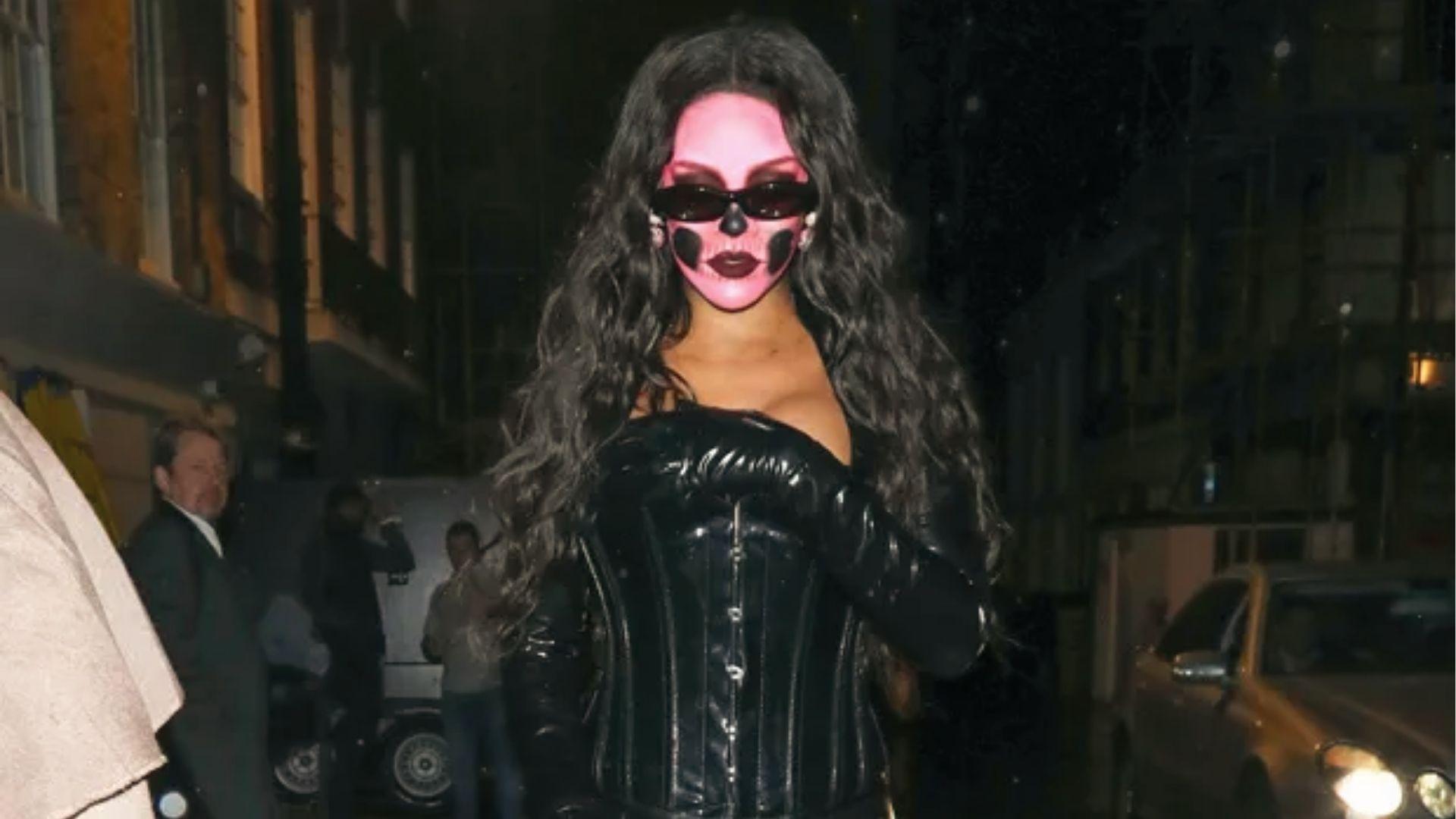 Rihanna in black latex corset with pink skull face paint and sunglasses.