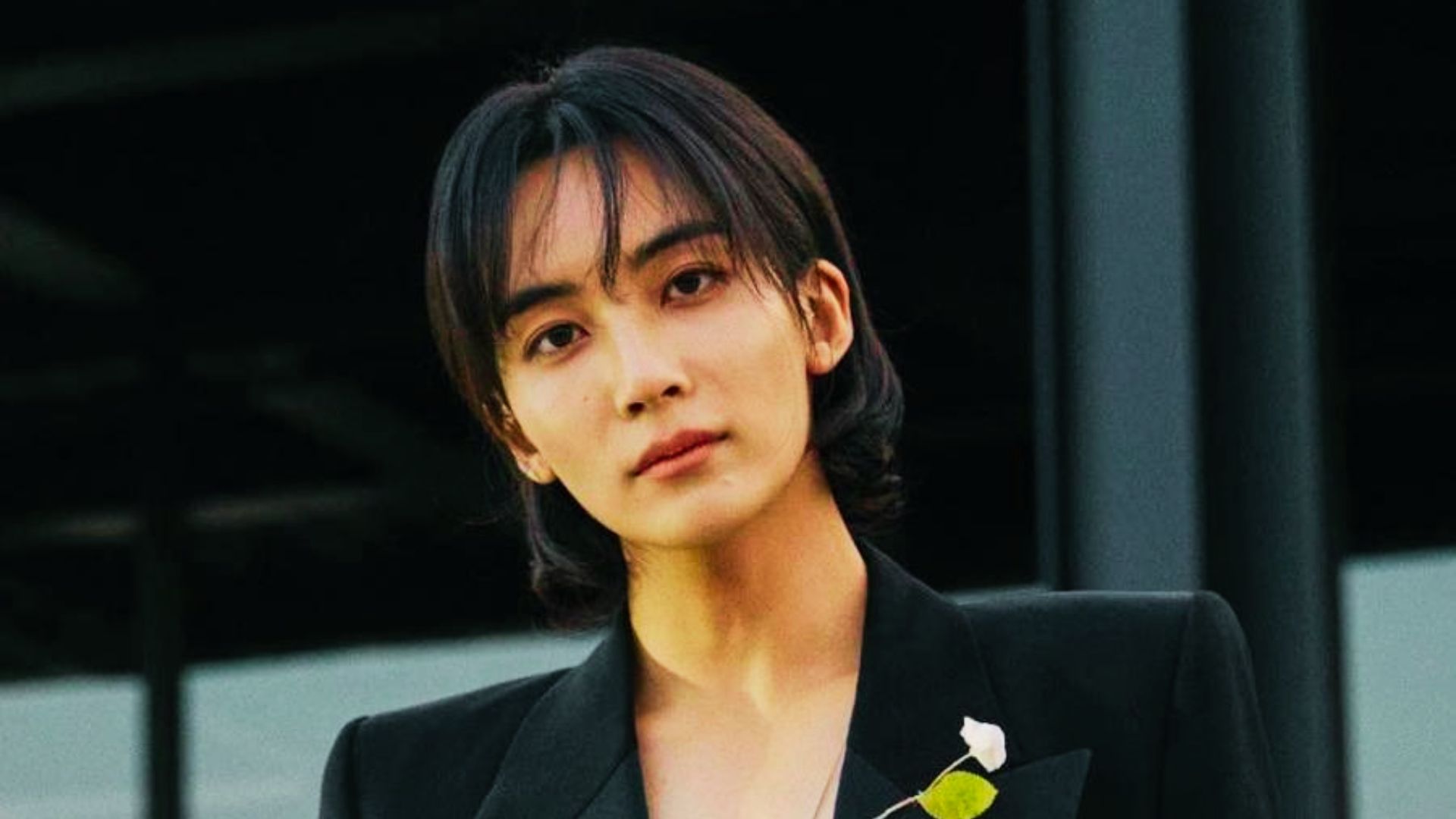 Jeonghan in a sharp black suit with a white flower pin, dark mid-length hair styled with curtain bangs.