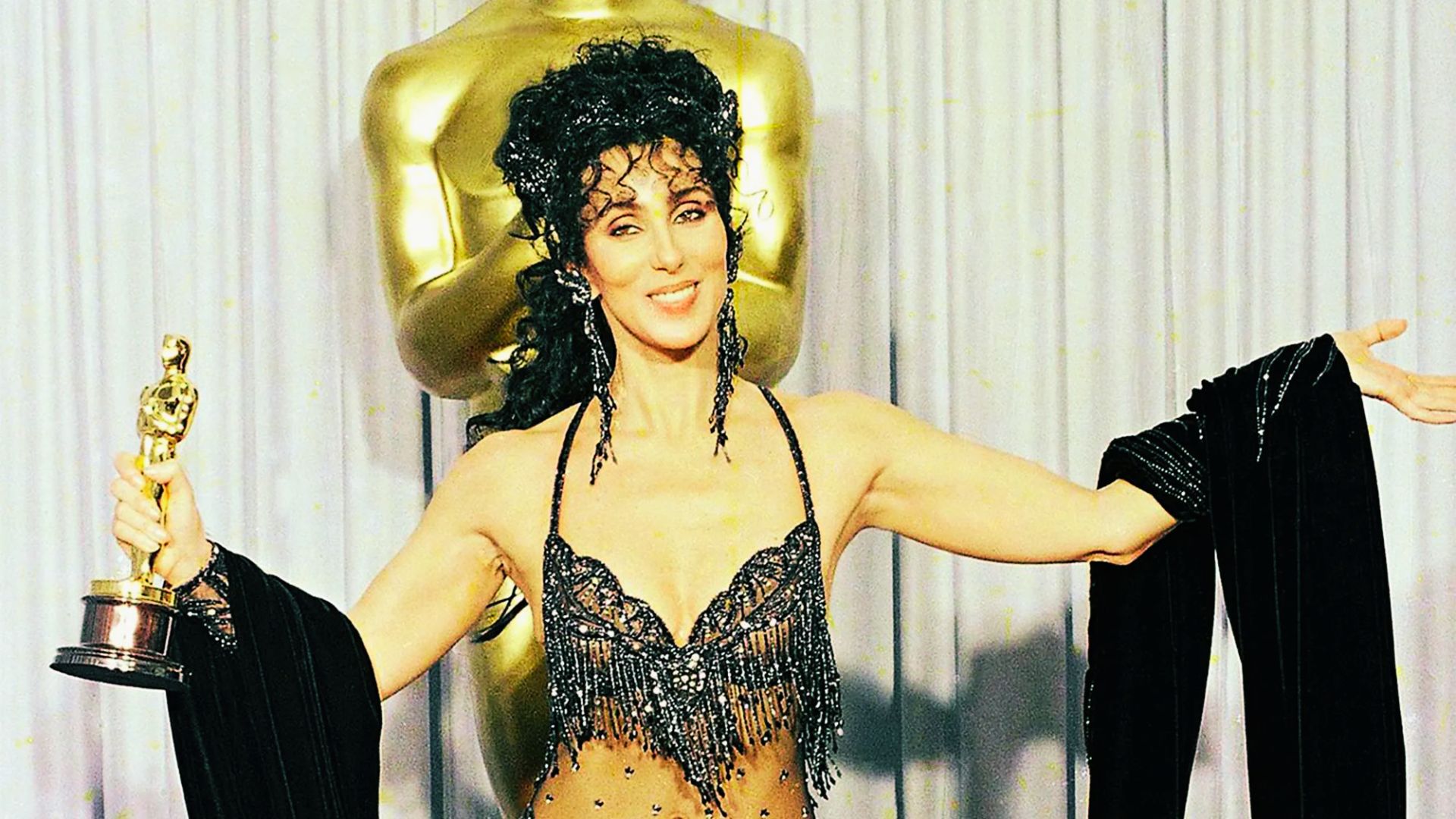 Cher on the red carpet in an elaborate white beaded headpiece shaped like a heart.