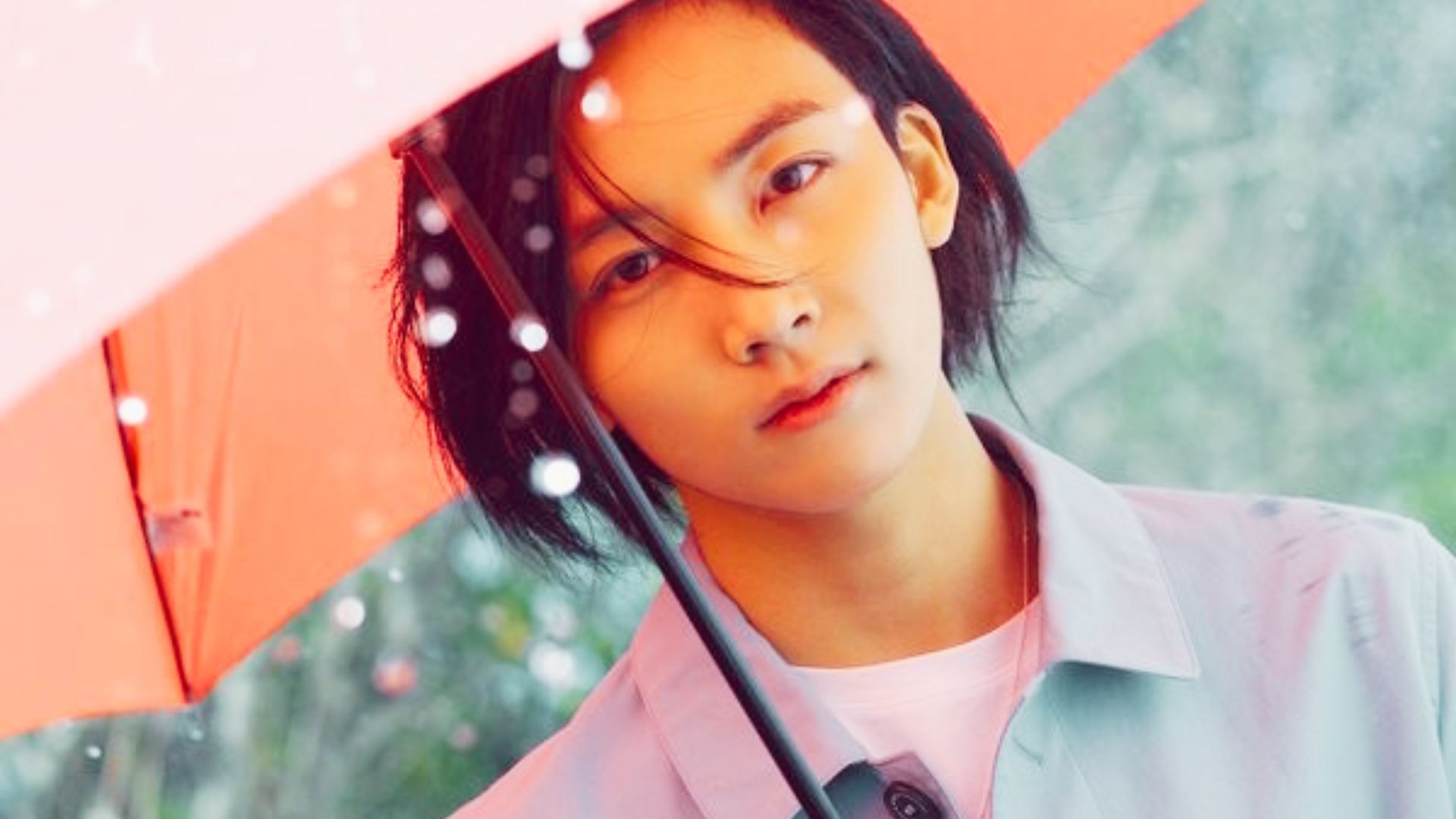 Jeonghan under a pink umbrella, dark hair damp from rain and framing his face.