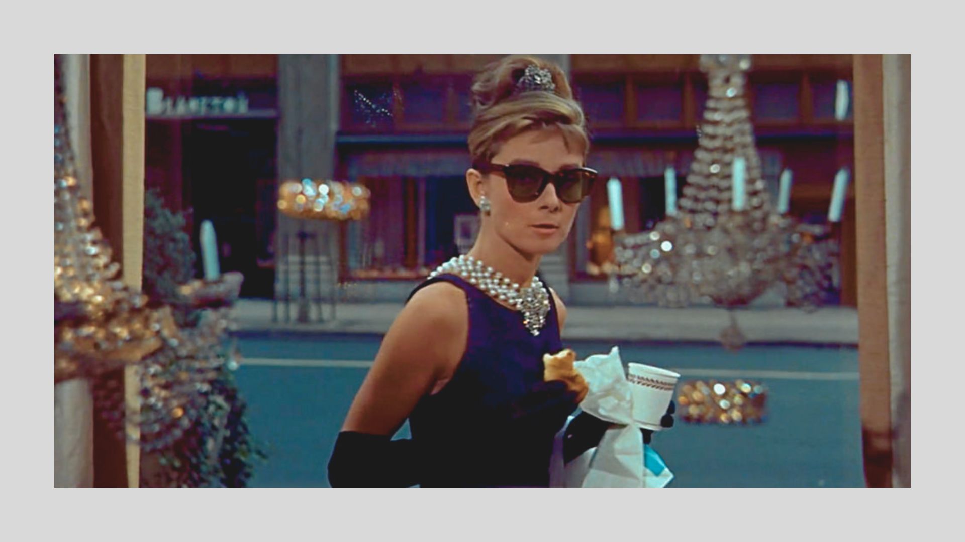 Audrey Hepburn as Holly Golightly in Breakfast at Tiffany's wears a sleeveless black Givenchy dress, layered pearl necklace, and oversized sunglasses.