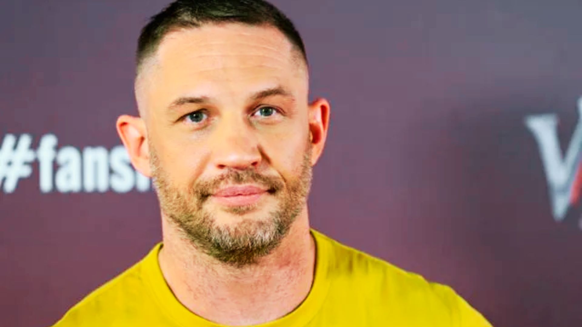 Tom Hardy wearing a yellow shirt with a tight buzz cut and high fade.
