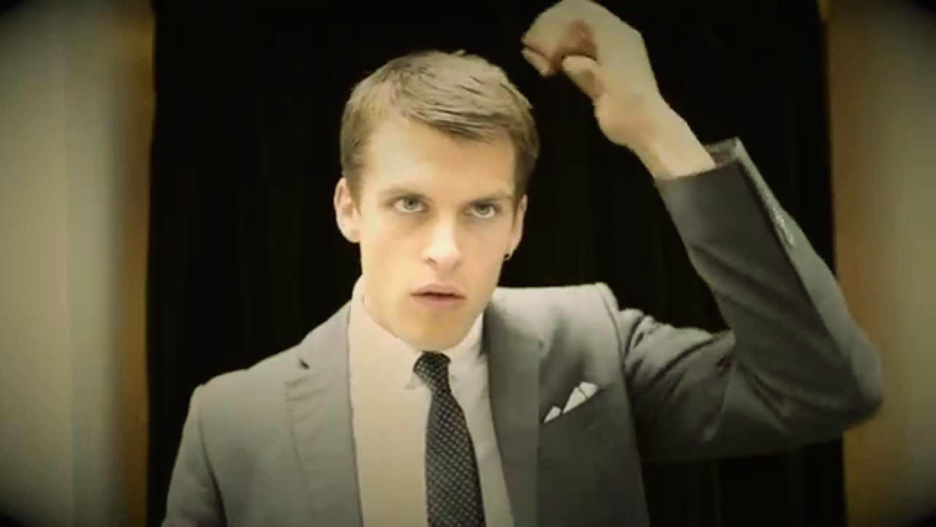 "A man in a suit and tie is holding his hair, appearing thoughtful or stressed in a professional setting."