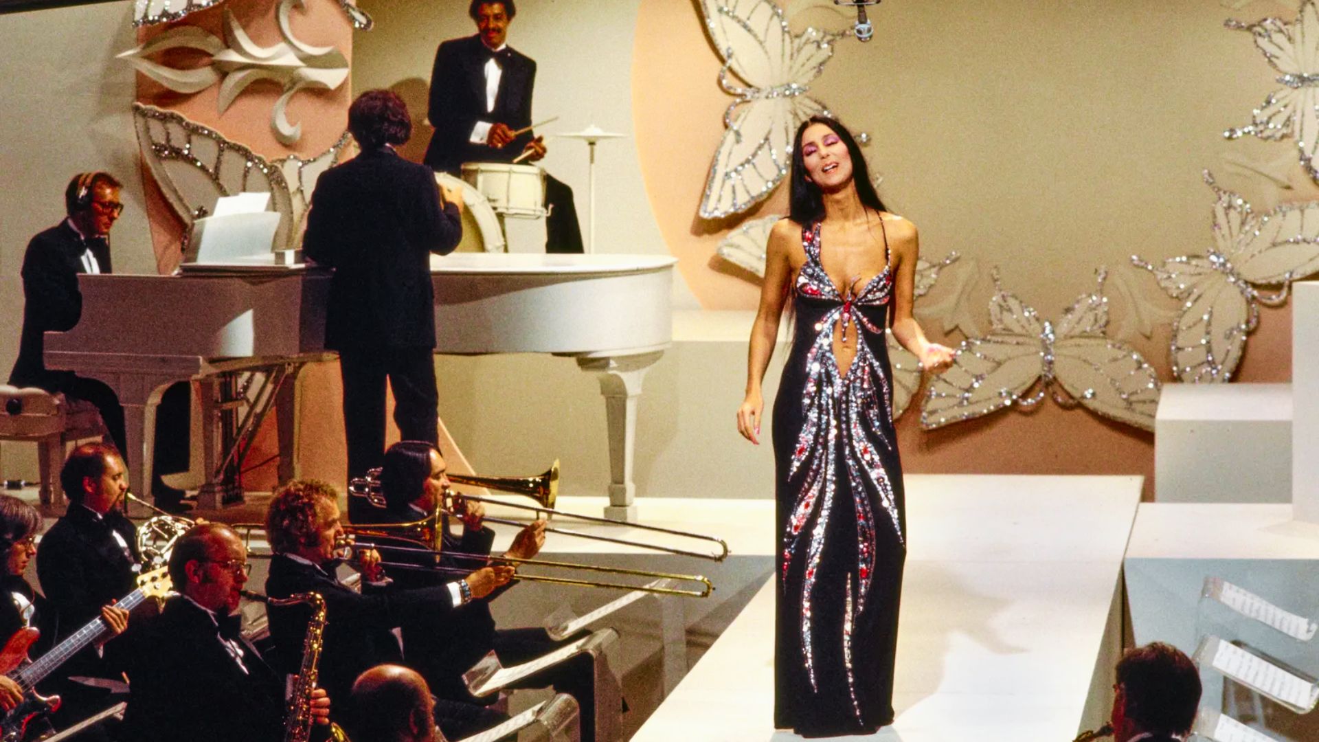 Cher performing on The Cher Show in 1975, wearing a black sequined gown with a butterfly-influenced design.