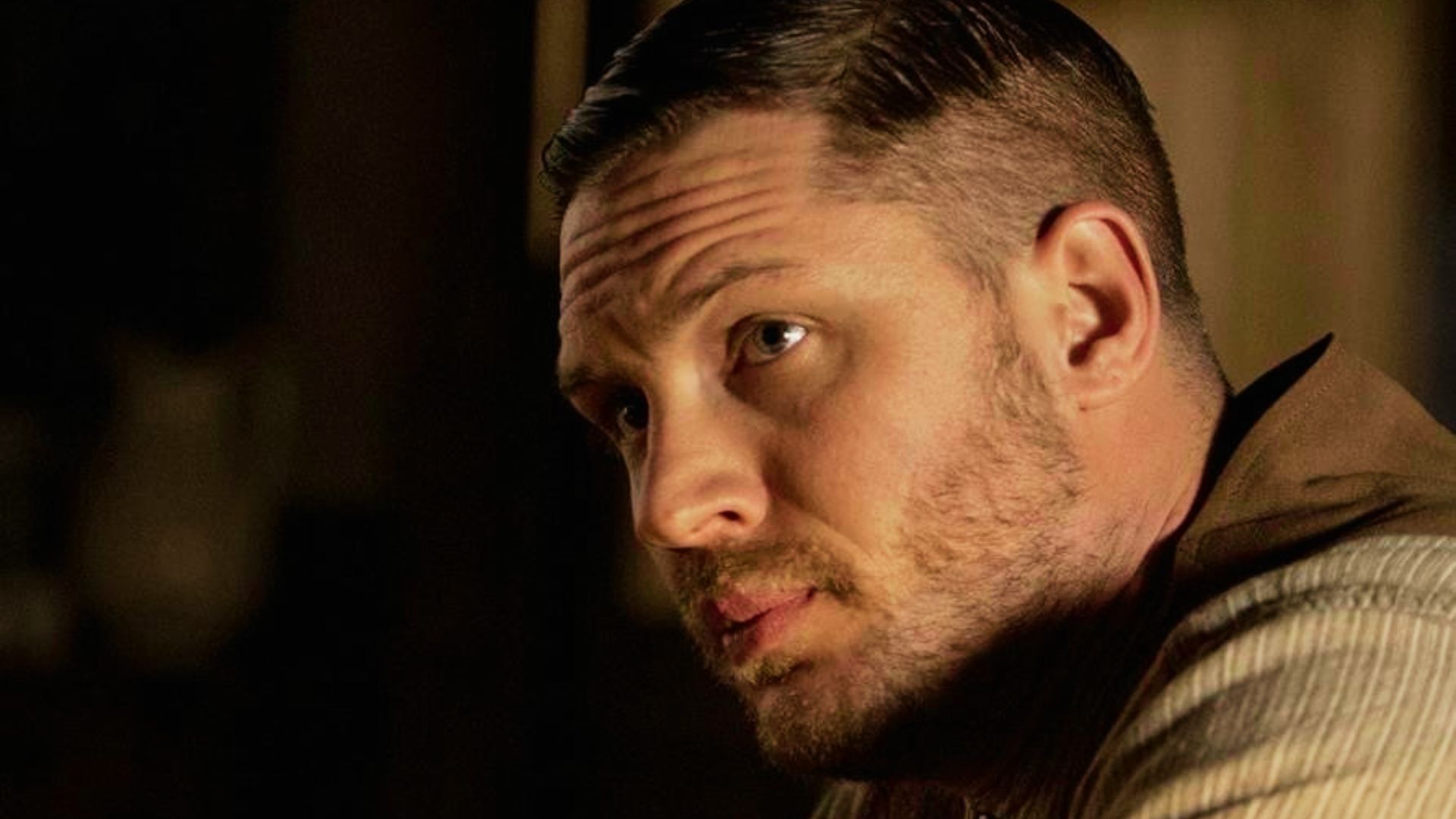 Tom Hardy with a sharp undercut and slicked back top, paired with a short beard.