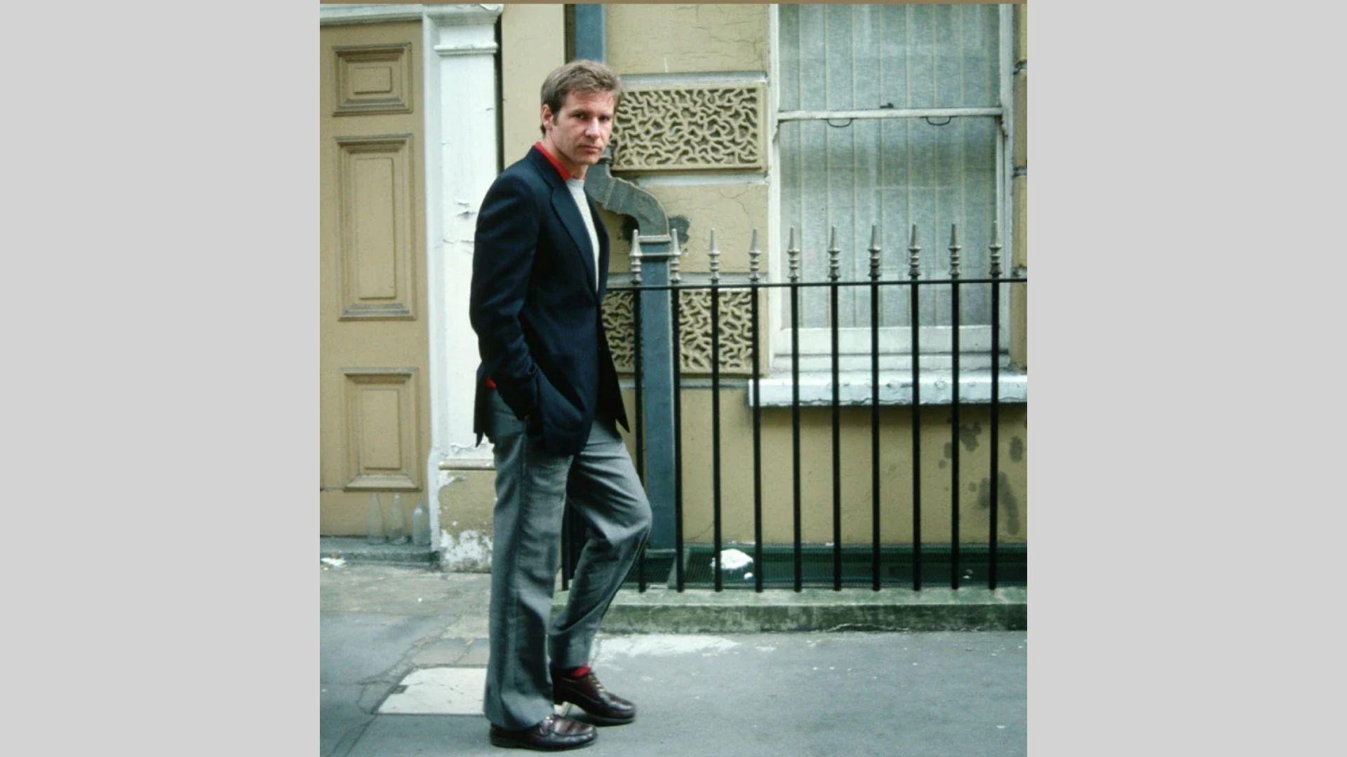 Younger Harrison Ford poses on sidewalk in navy blazer, gray pants, and brown shoes