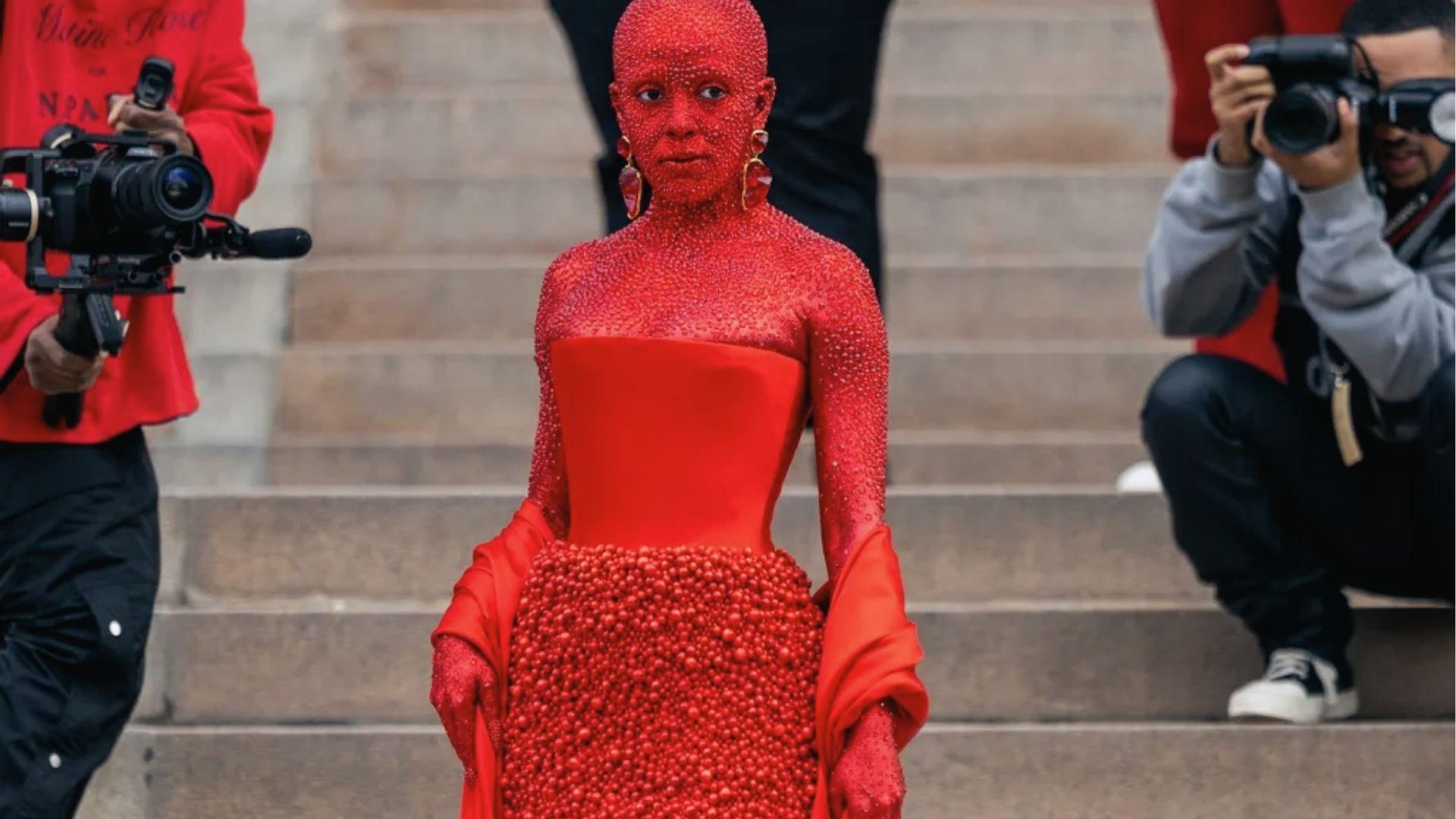 Doja Cat covered in red crystals wearing strapless red gown on steps.