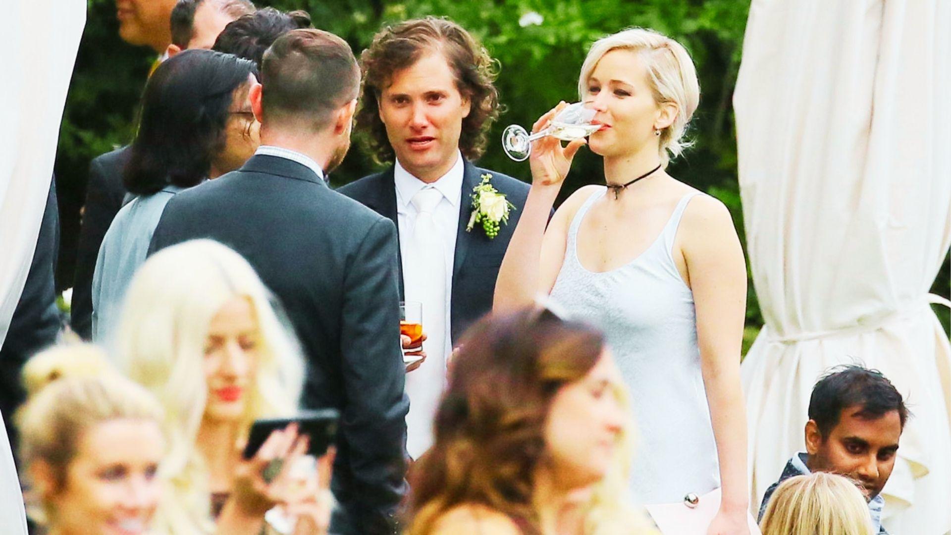 Blonde actress sips champagne in light blue dress at crowded outdoor wedding reception party