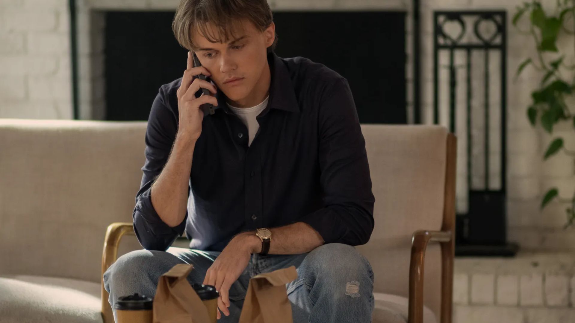 Conrad sits indoors on a call in a navy button-up over a white tee with light wash jeans.