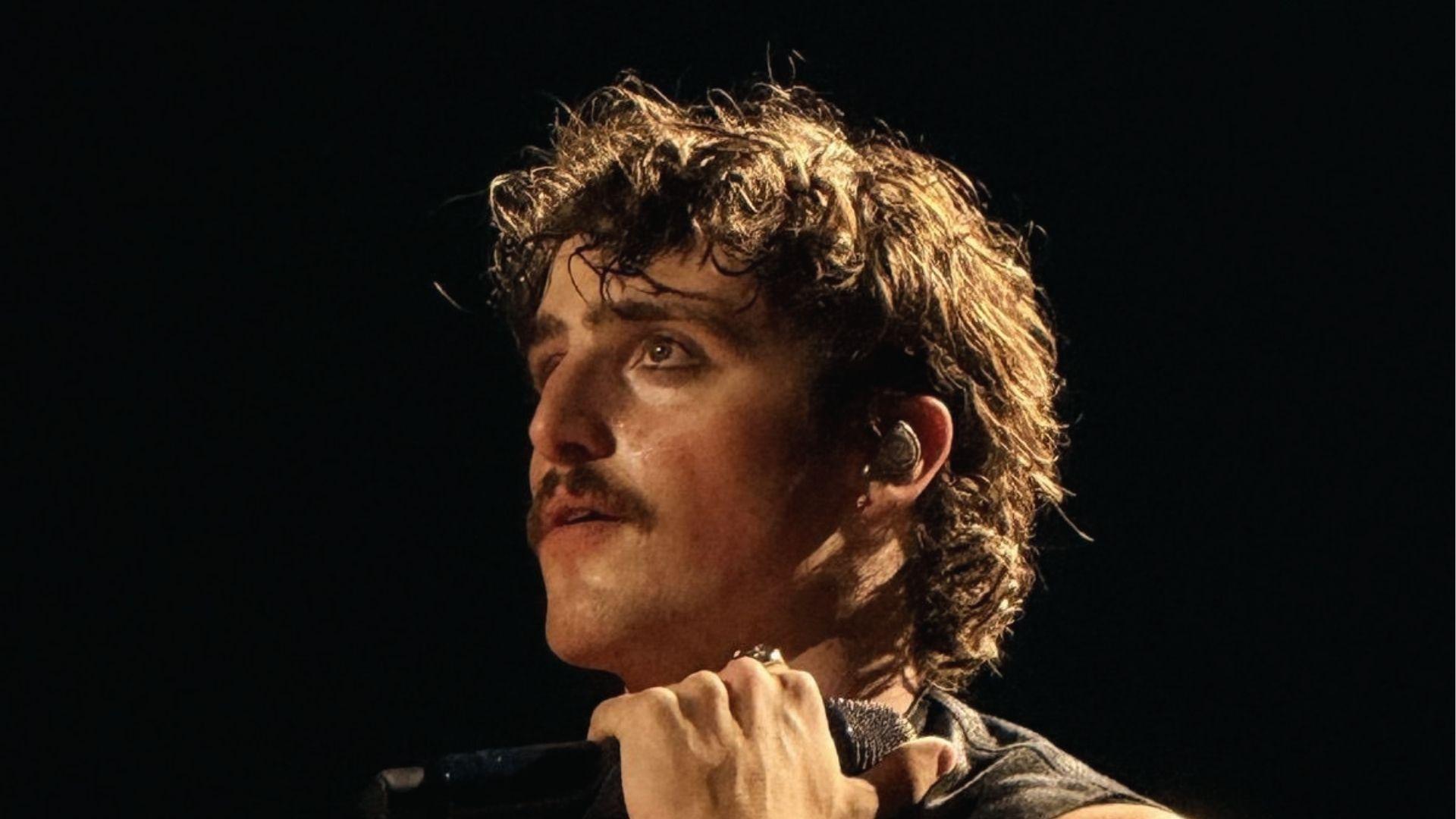 Benson Boone on stage with sweaty tousled curly mullet lit by spotlight.