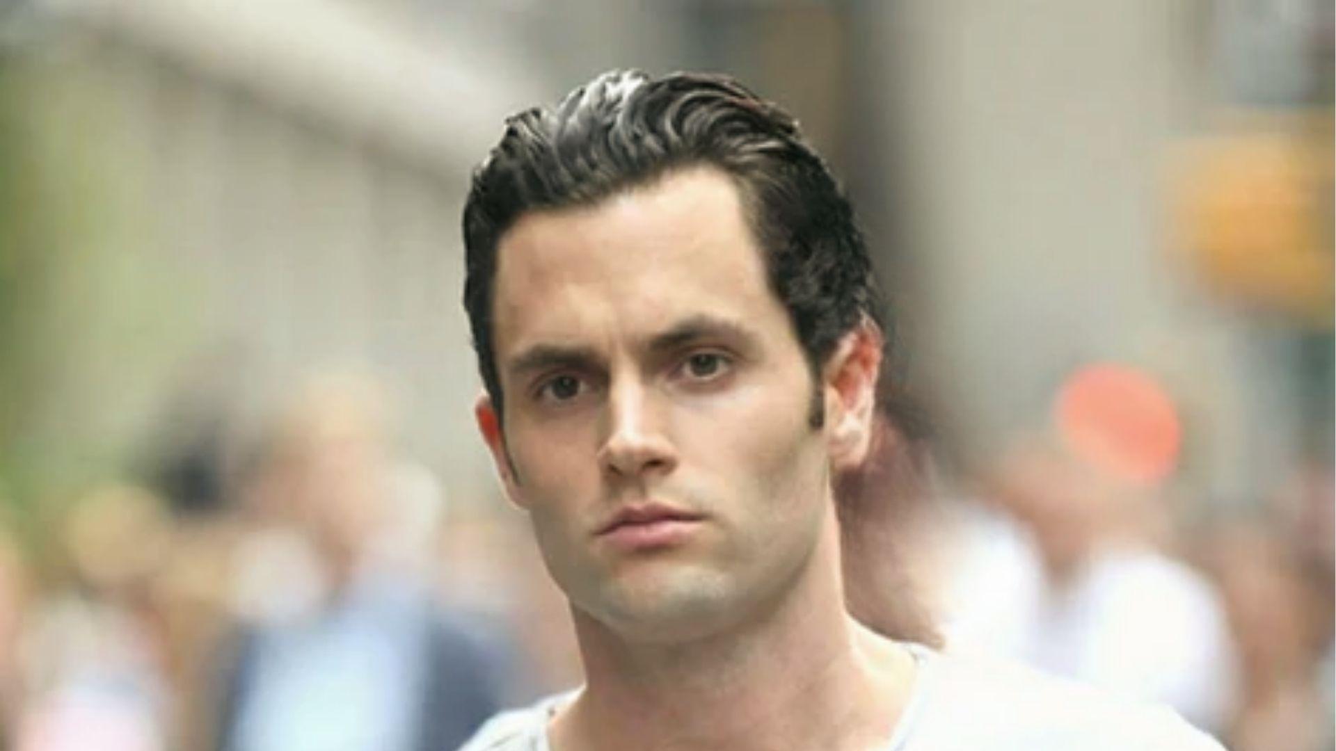 Penn Badgley styles slicked-back short hair with slight wave walking outdoors city scene.