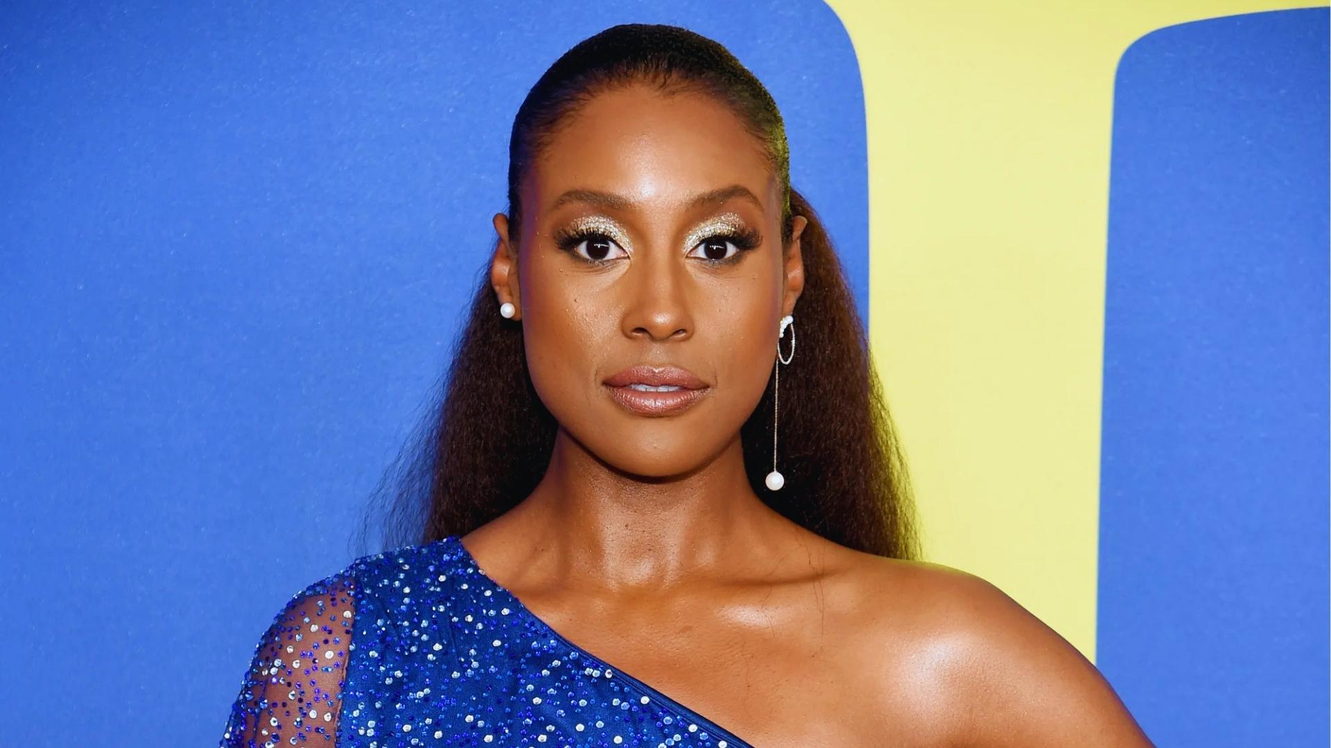 Issa Rae wears a sleek low ponytail with long textured extensions and glitter eyeshadow on the red carpet.